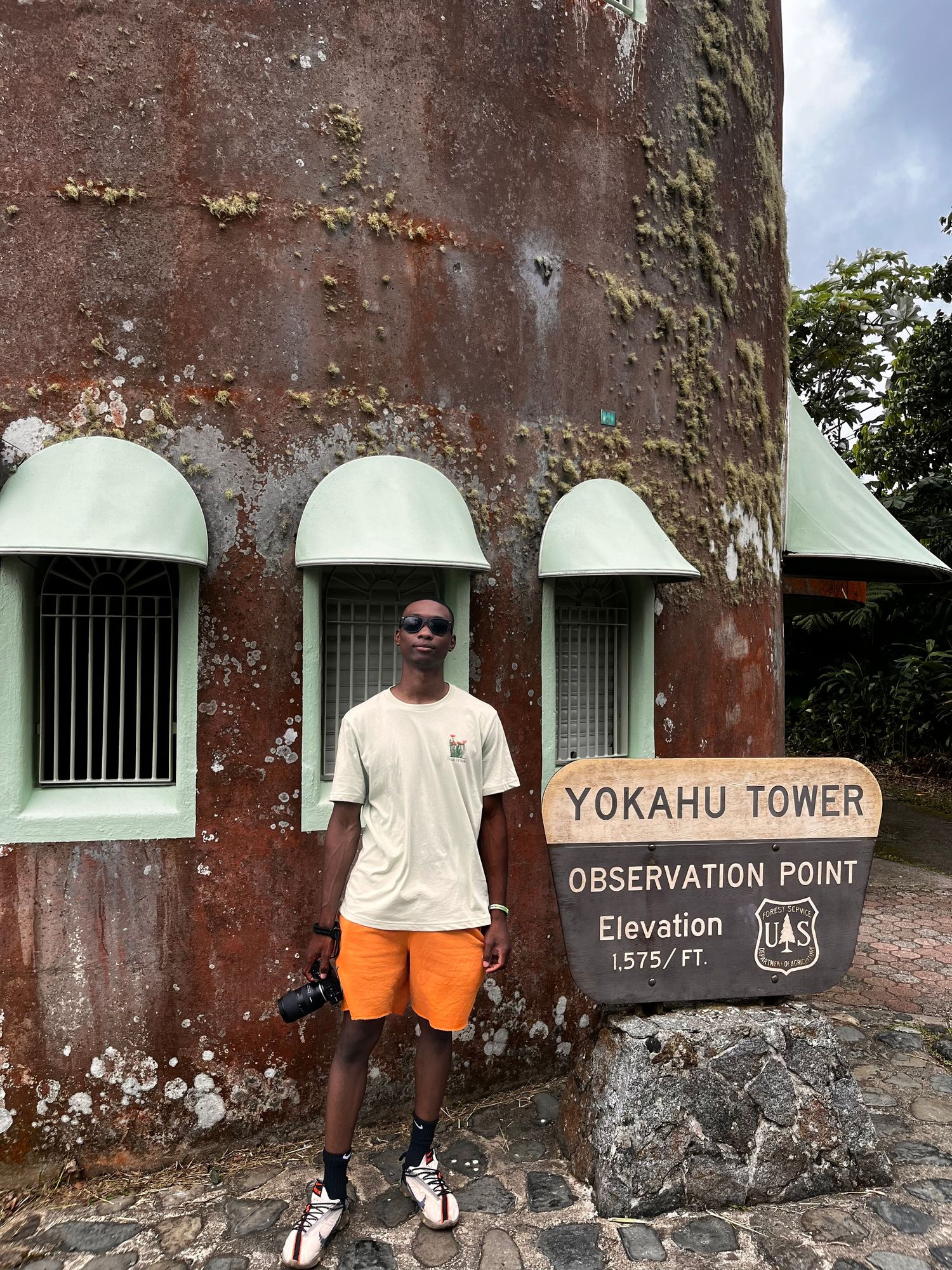 Tourist posing at Yokahu Tower observation point wearing orange shorts and white t-shirt.