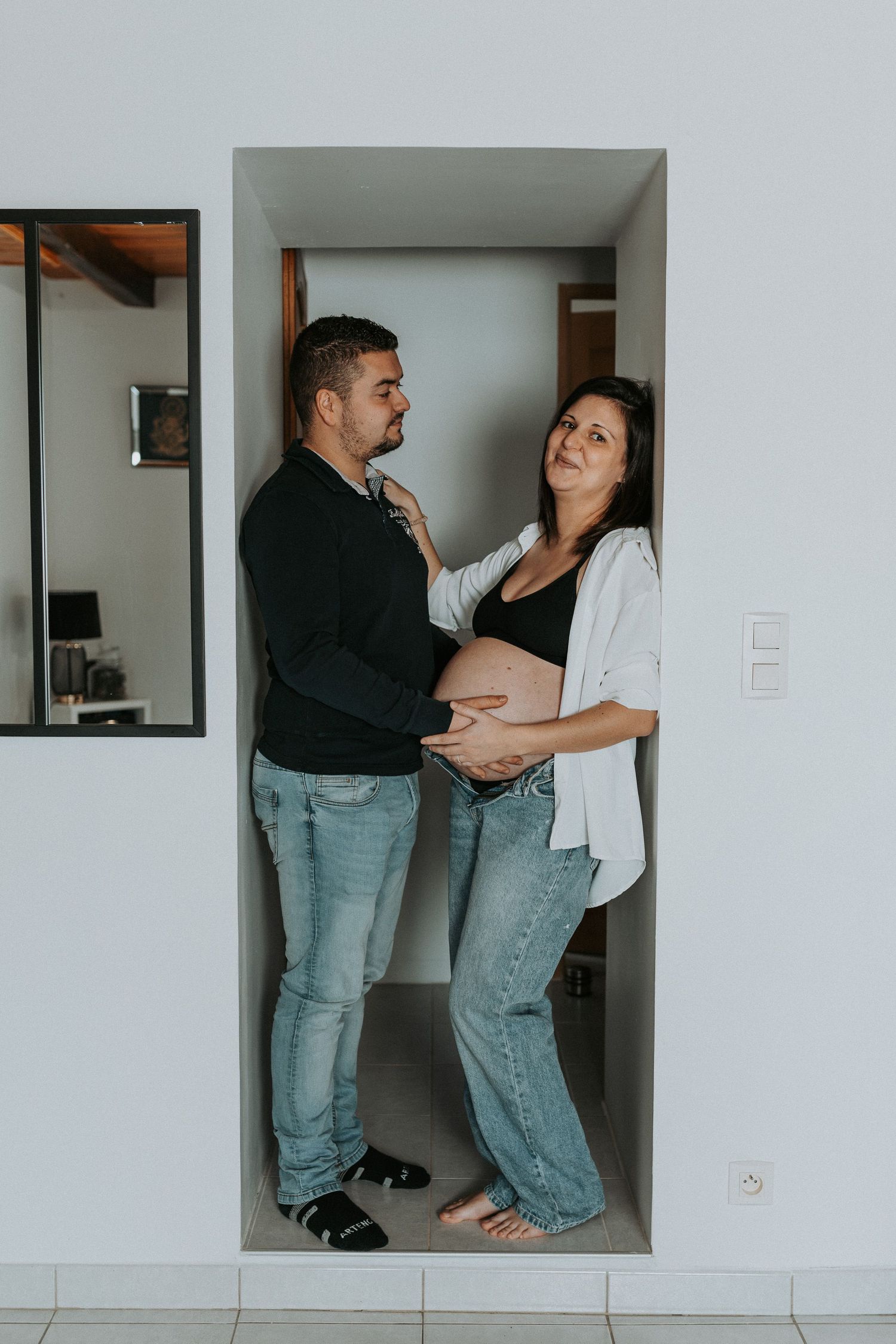 Two people in casual denim jeans and t-shirts dance playfully together against a white wall.