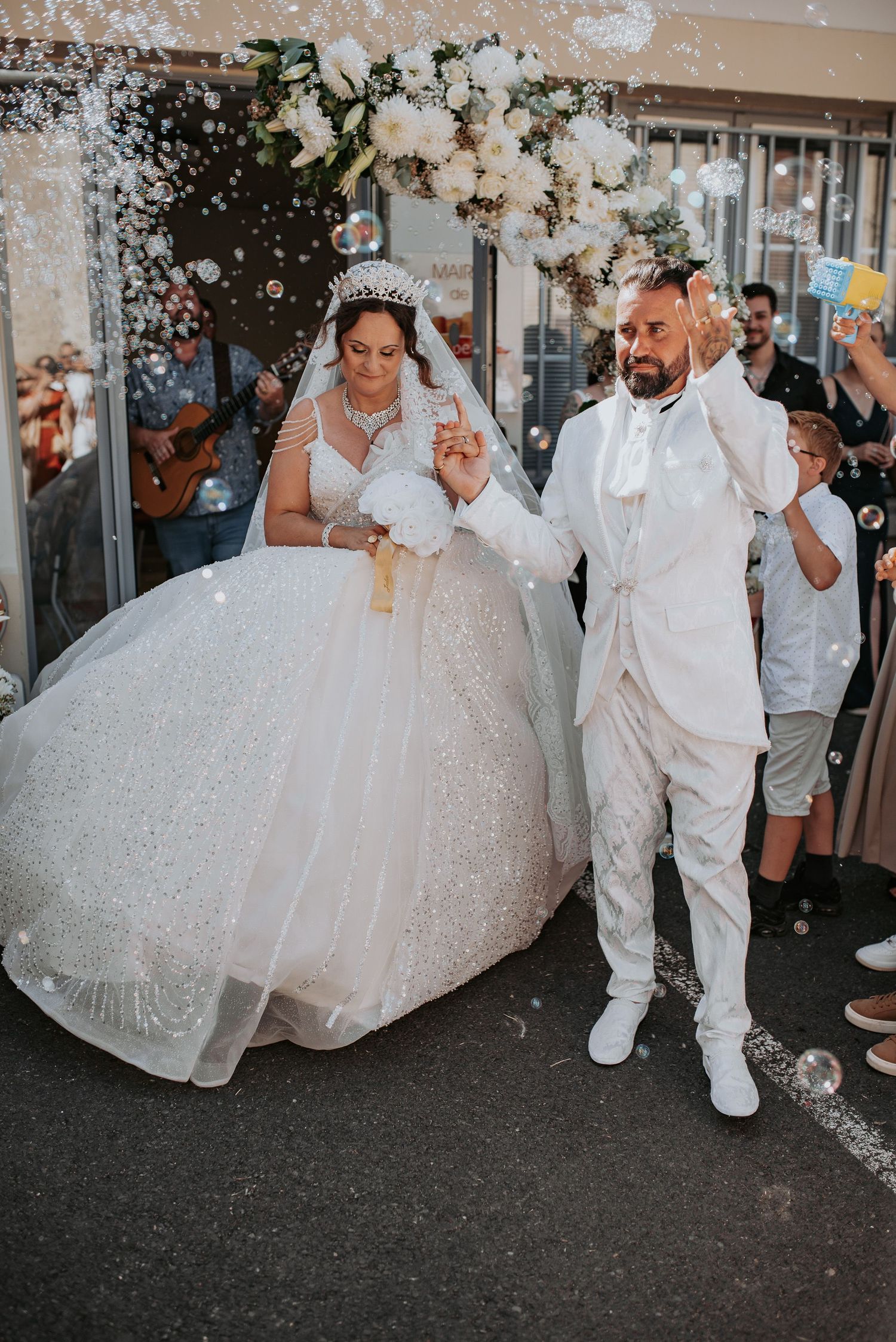 Newlyweds in white attire dance and celebrate during their wedding reception as guests shower them with confetti.