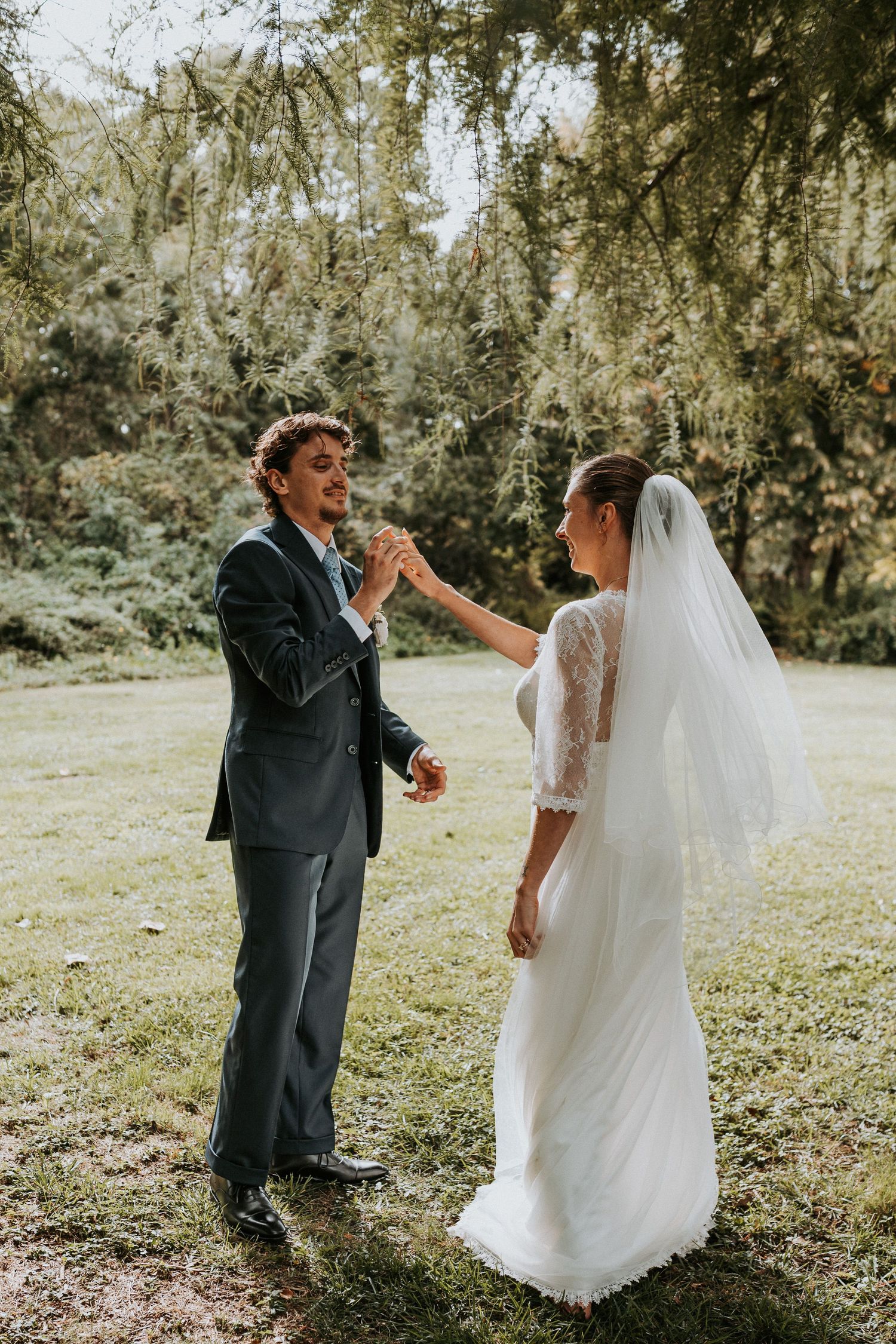 A romantic outdoor wedding moment captured in a sunlit garden with hanging willow trees and natural greenery.