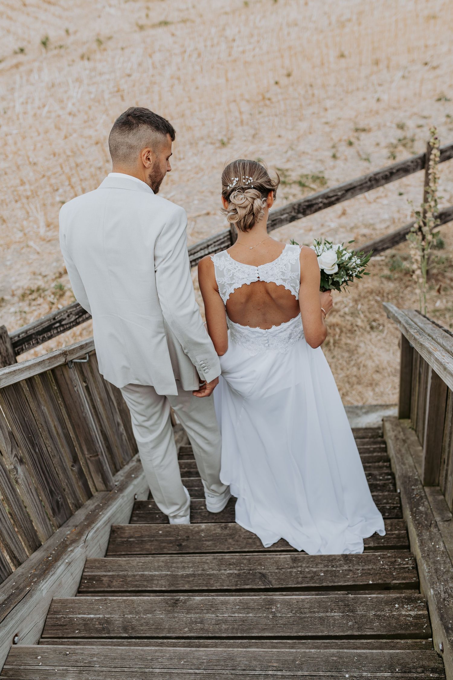 A couple in wedding attire descending rustic wooden stairs together in a romantic outdoor setting.