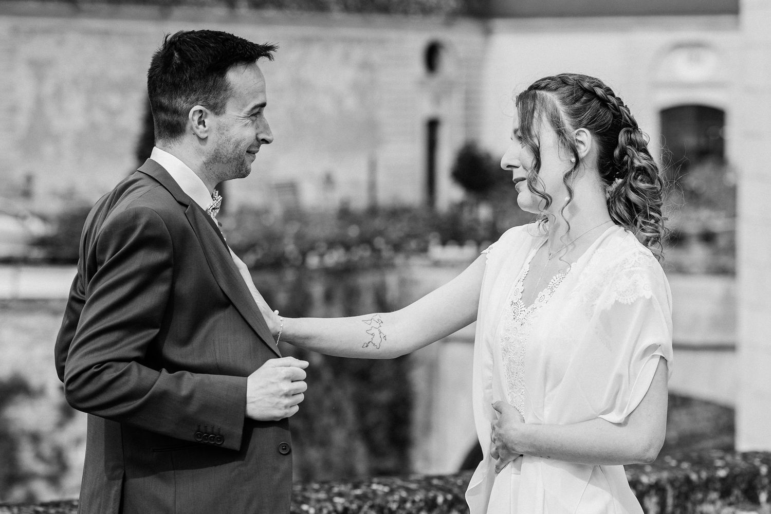 Black and white photo of smiling bride and groom sharing a tender moment outdoors during their wedding ceremony.