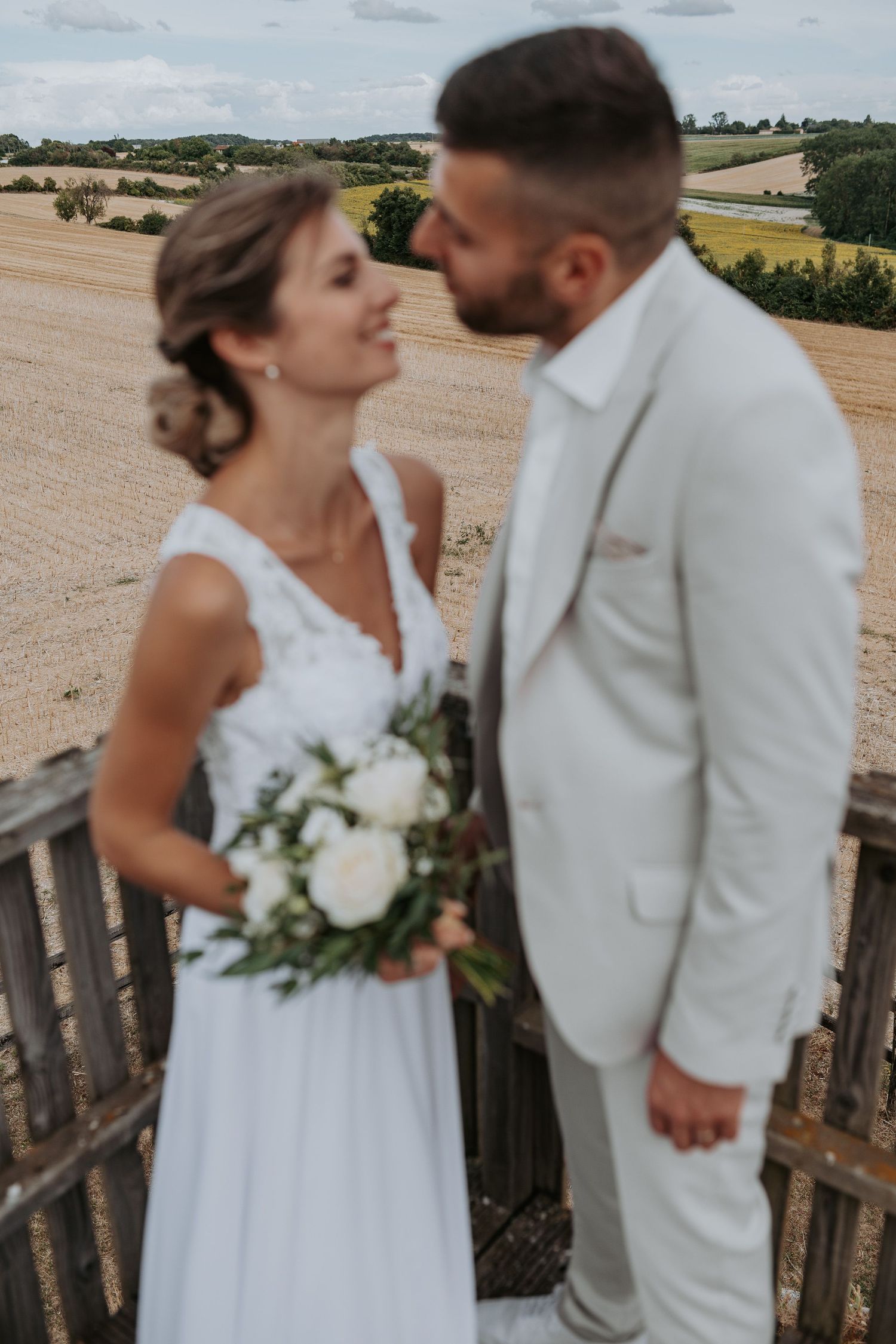 A romantic wedding couple shares intimate moments in a rustic outdoor setting with rolling countryside views in the background.
