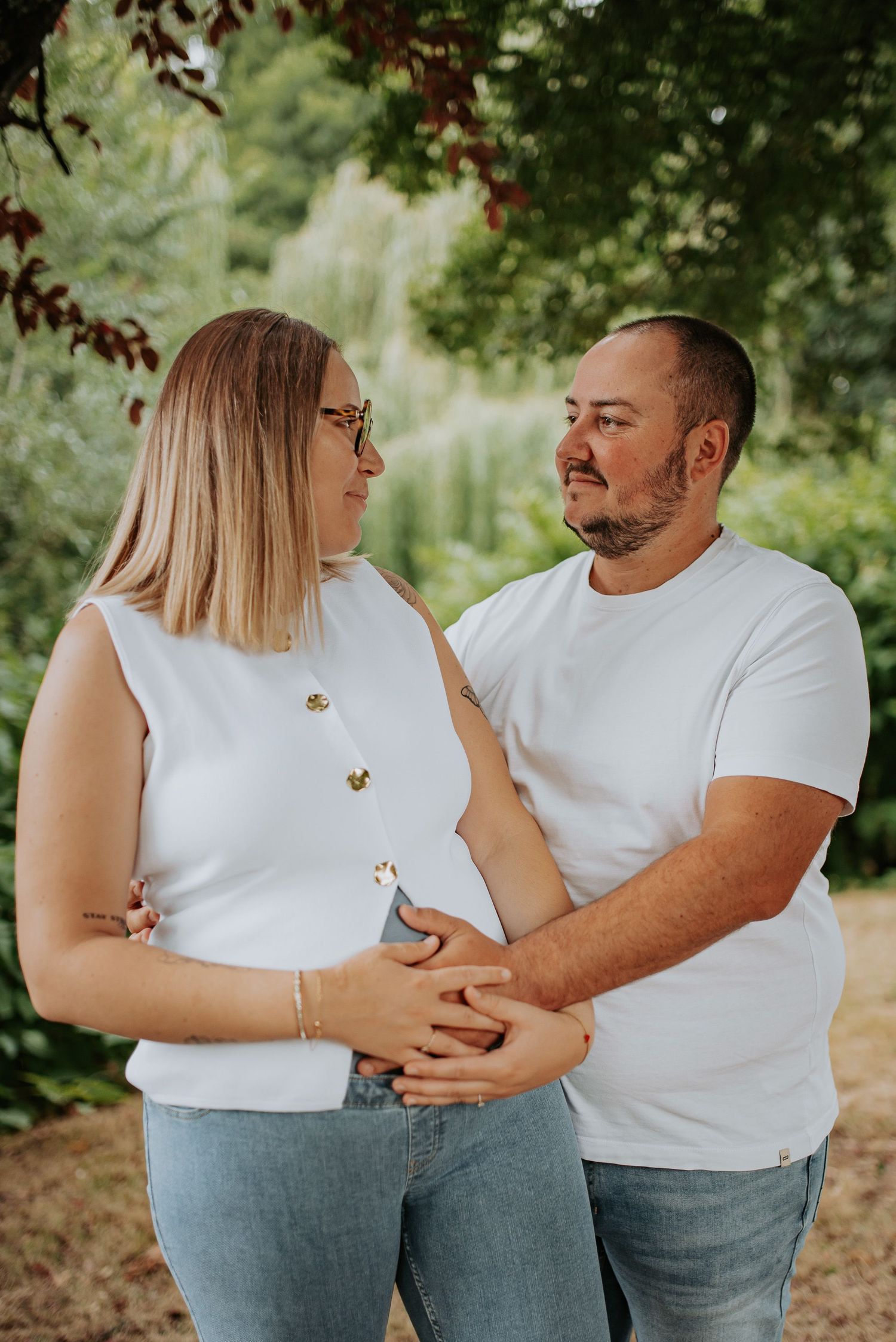A couple in white shirts share an intimate moment together in a garden setting, glowing with happiness.