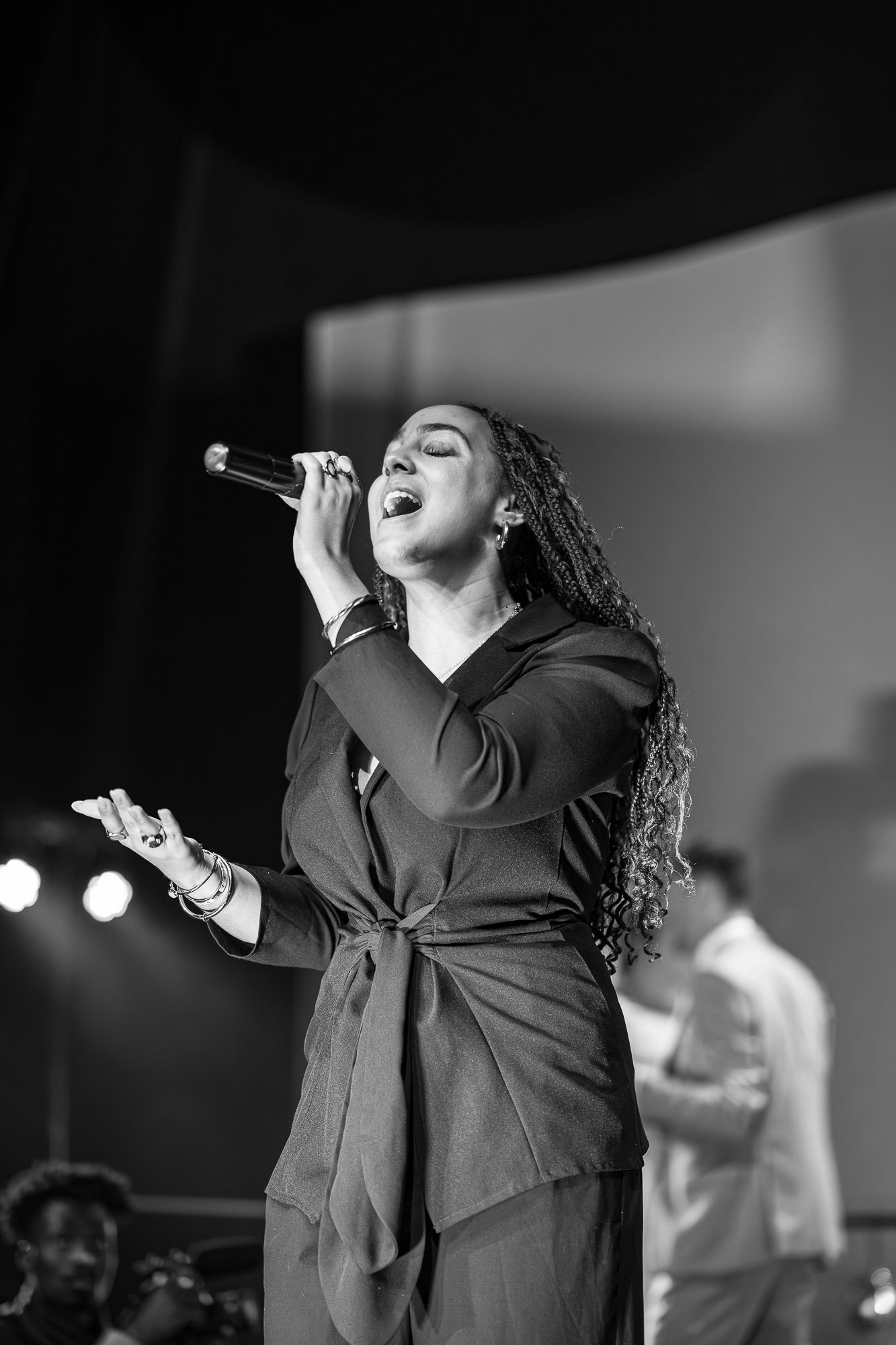 A performer in black attire sings passionately on stage during a dramatic musical performance.