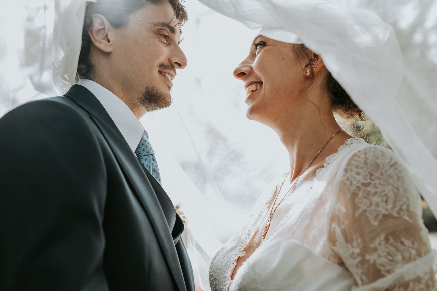 A joyful bride and groom share an intimate moment under a white canopy during their outdoor wedding ceremony.