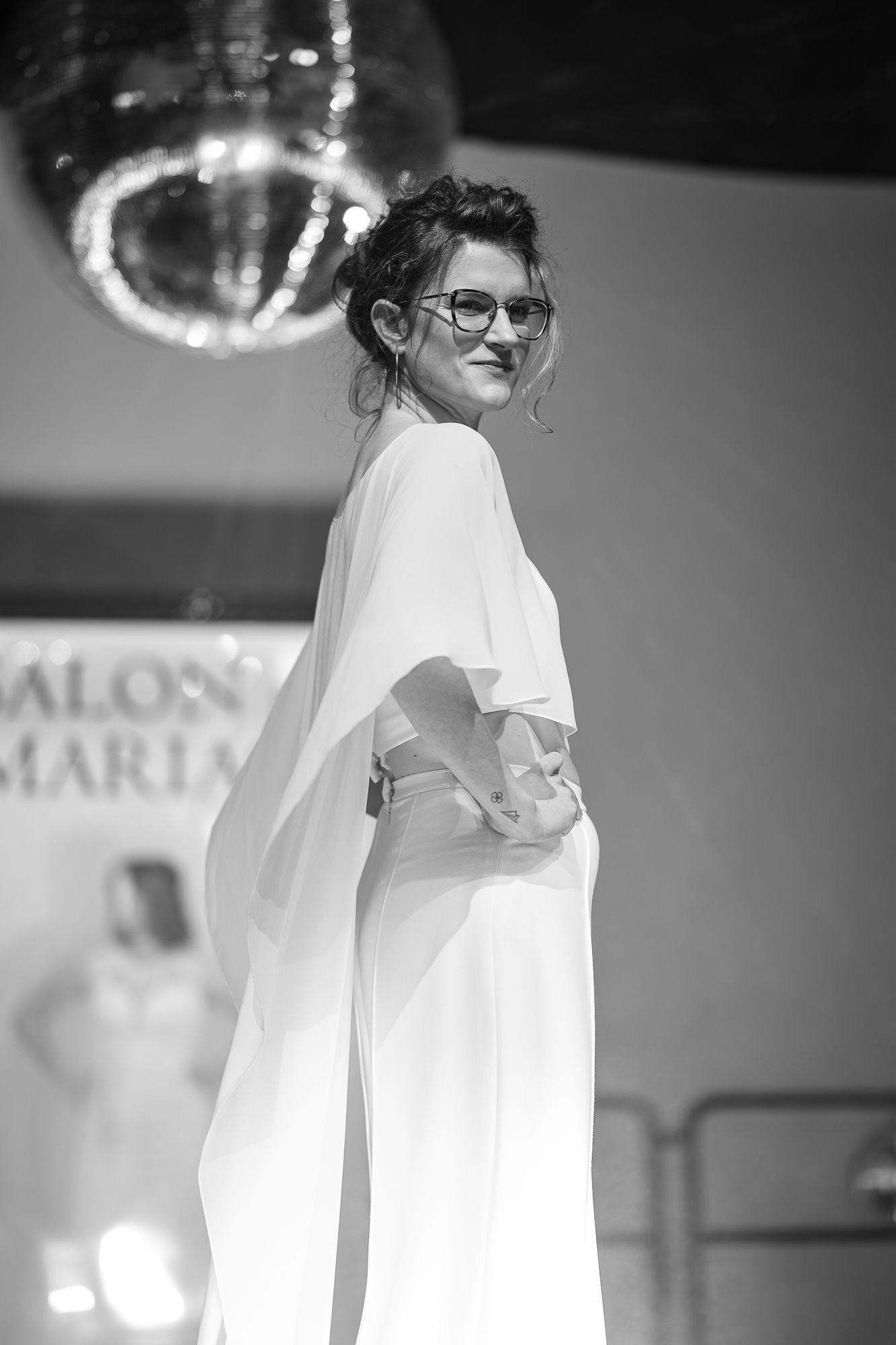 A person in a white t-shirt and glasses smiles while standing against a blurred background.
