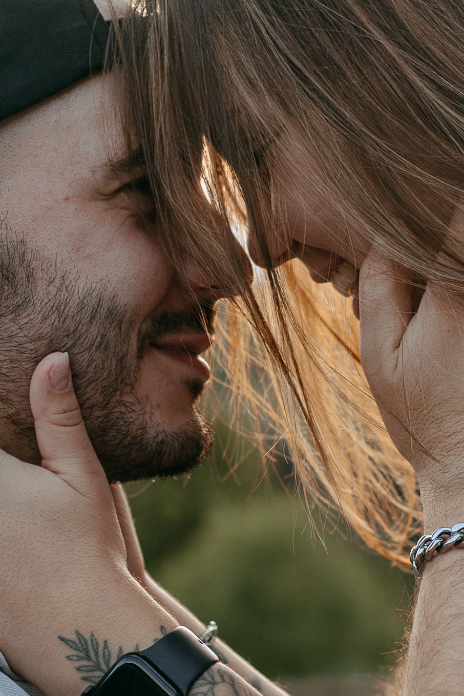 Intimate close-up portrait of a couple sharing a tender moment in golden sunlight, with long hair catching the glow.