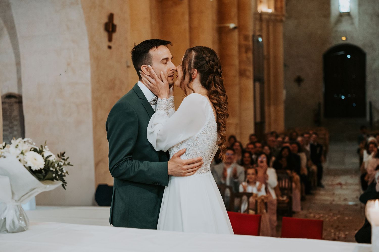 Bride and groom share their first kiss at the altar during a romantic church wedding ceremony with guests seated in pews.