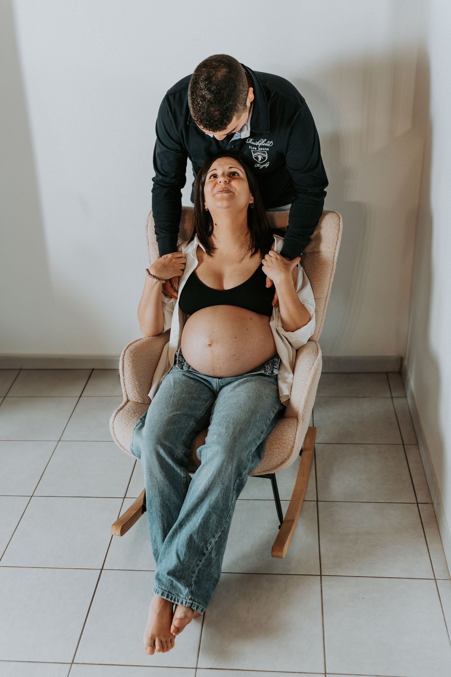 A sequence of photos showing a person in jeans sitting in a wooden chair on a tiled floor during a maternity photoshoot.