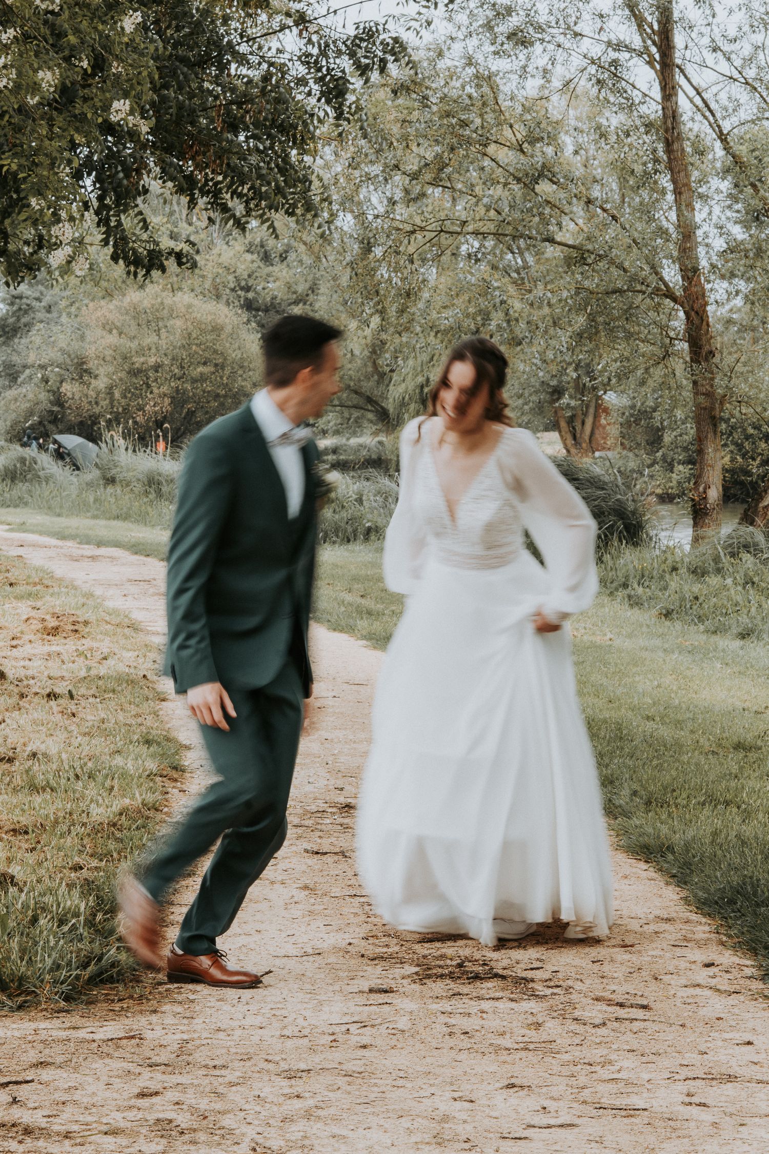 Bride and groom walking hand in hand on a garden path, smiling at each other in elegant wedding attire.