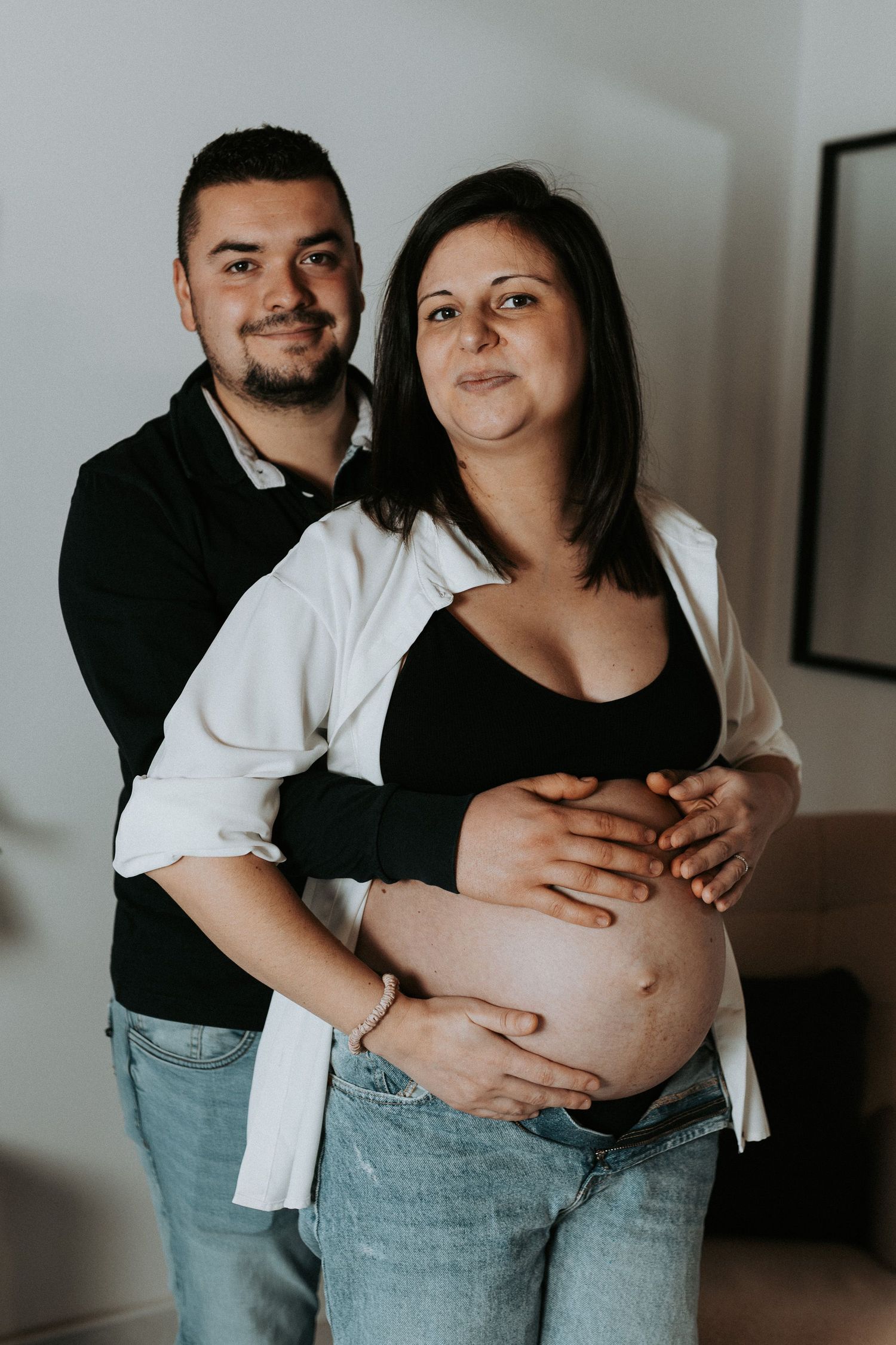 A couple embraces in a series of intimate maternity photos showing a pregnant belly in light and shadow.