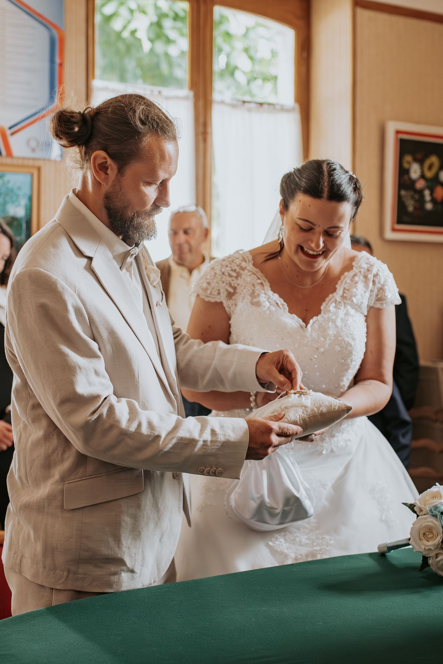 A couple participates in a marriage ceremony at an altar with a green table during a daytime indoor event.