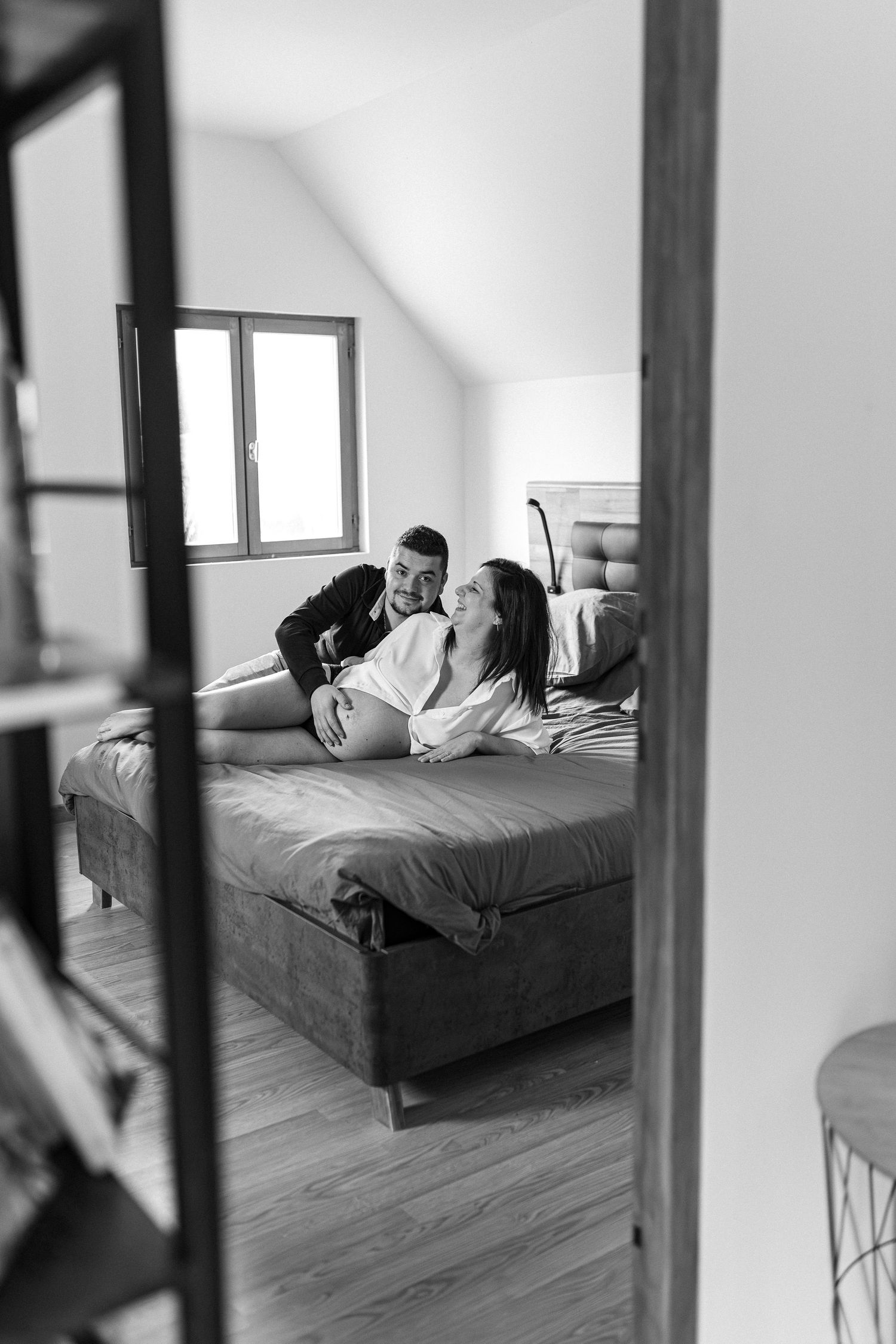 A minimalist bedroom with white walls and wooden floors shows a bed viewed through doorway frames.