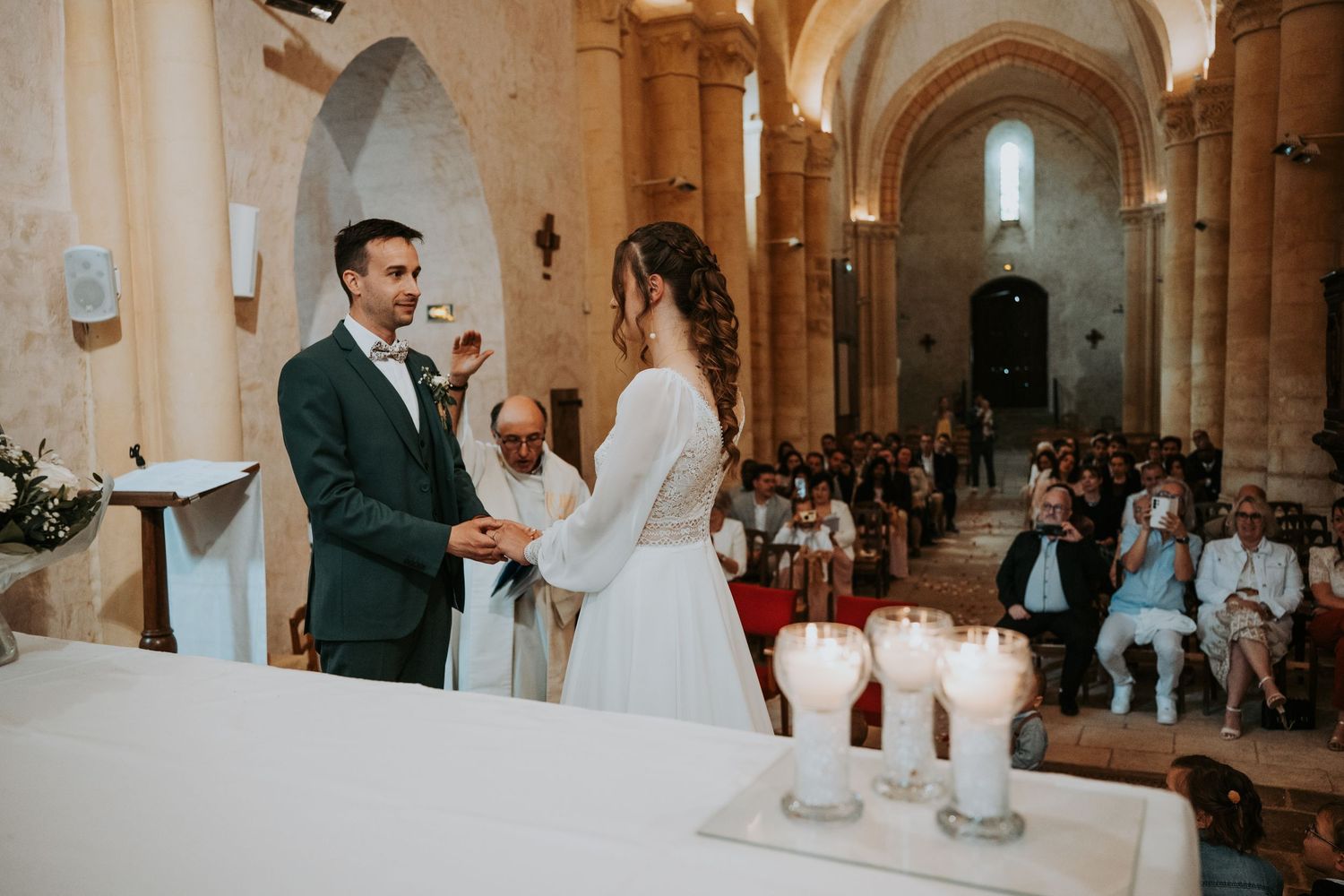 Couple exchanging vows at a church wedding ceremony with guests seated in pews and candles on the altar.