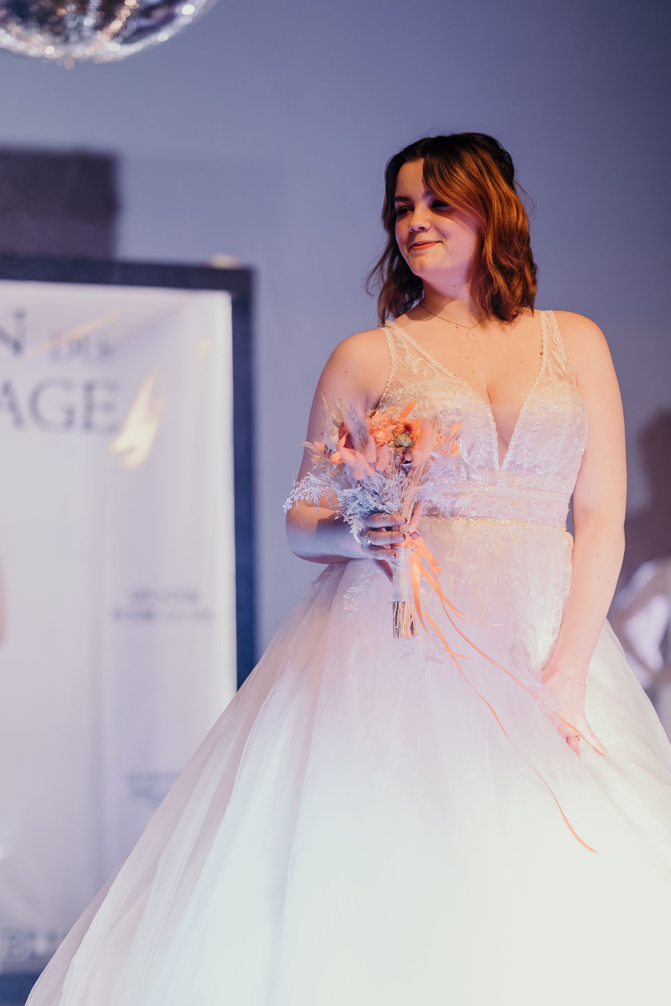 A model showcases an elegant white wedding dress with lace details and a full tulle skirt on a fashion runway.