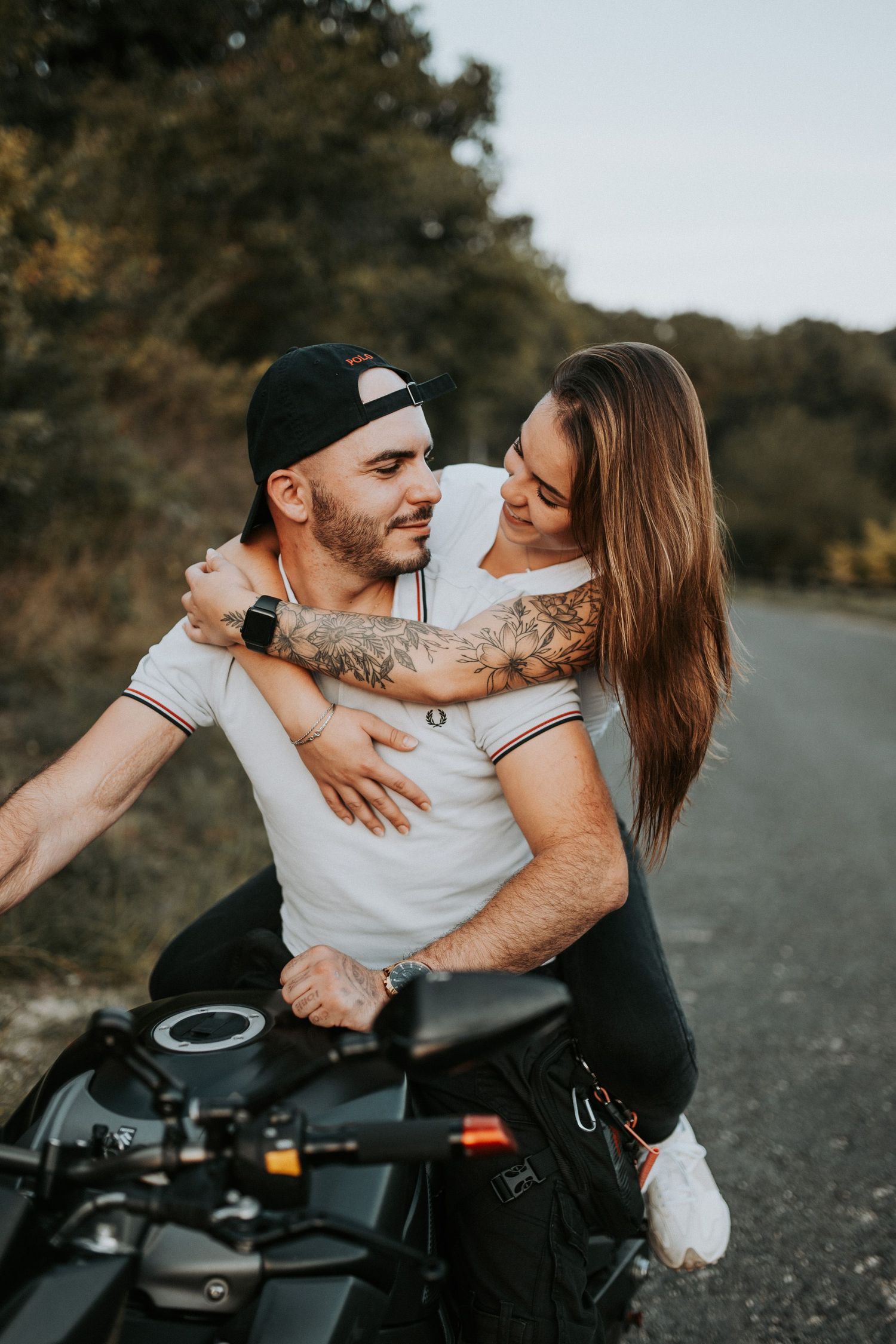 Romantic couple sharing intimate moments on a motorcycle on a rural road during a photoshoot.