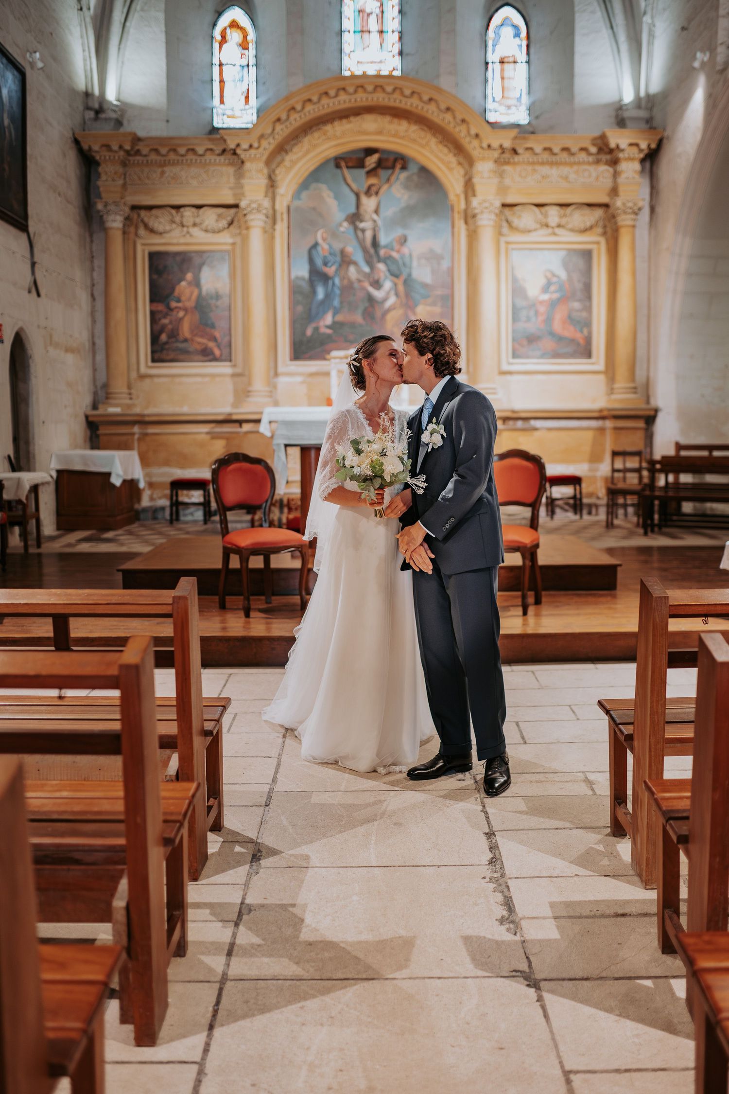 A romantic moment between newlyweds sharing a kiss in a beautiful church sanctuary with stained glass windows and wooden pews.