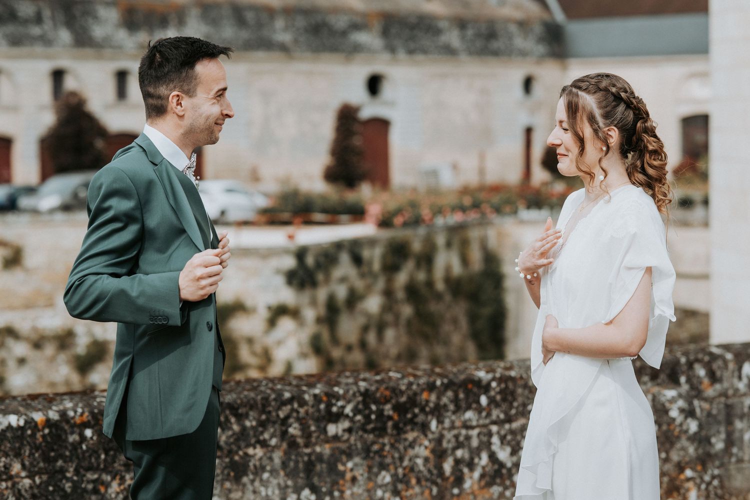 Bride and groom sharing a joyful moment outdoors at a wedding venue, dressed in white gown and green suit.