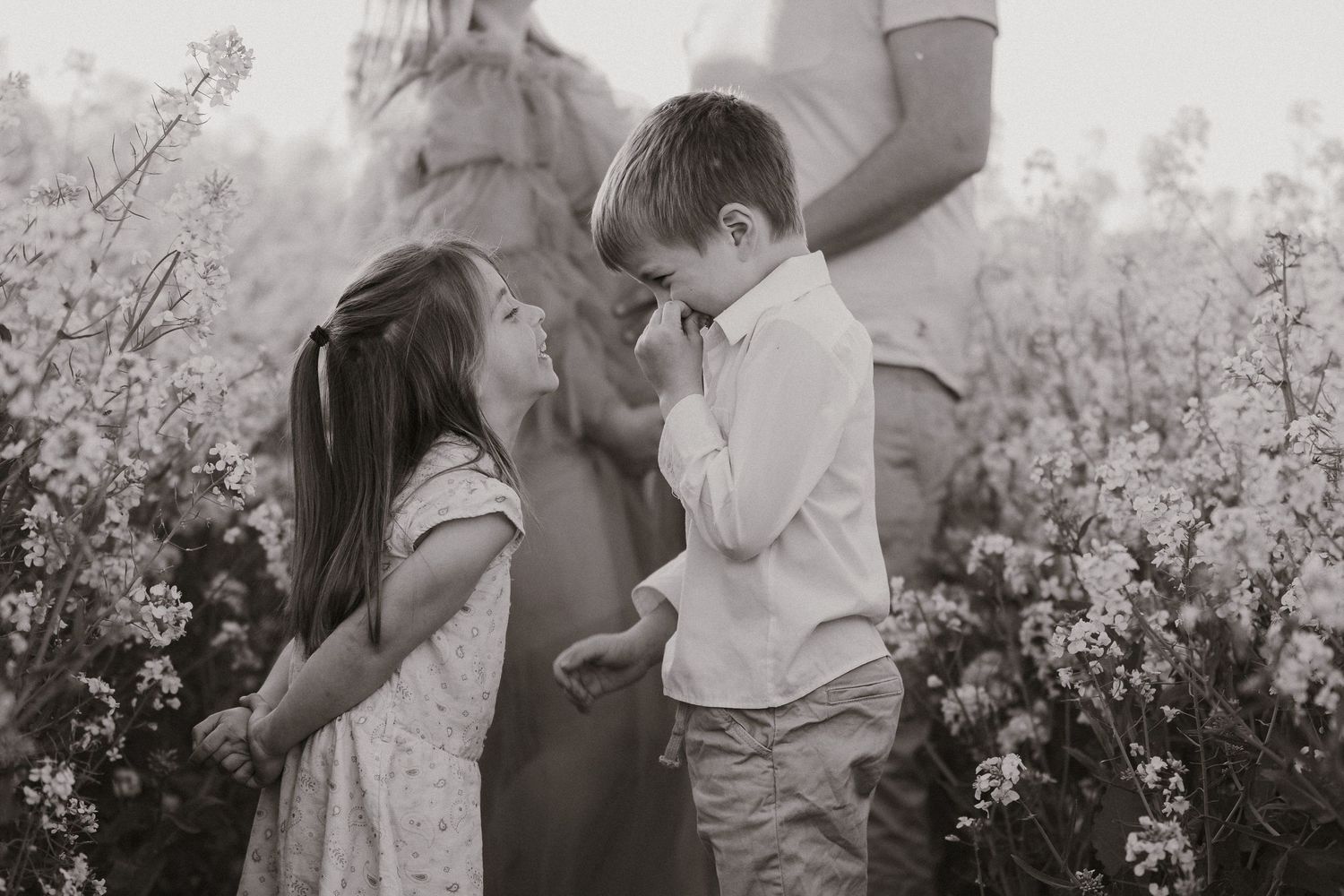 Black and white photo of two young children sharing a tender moment in a blooming flower field.