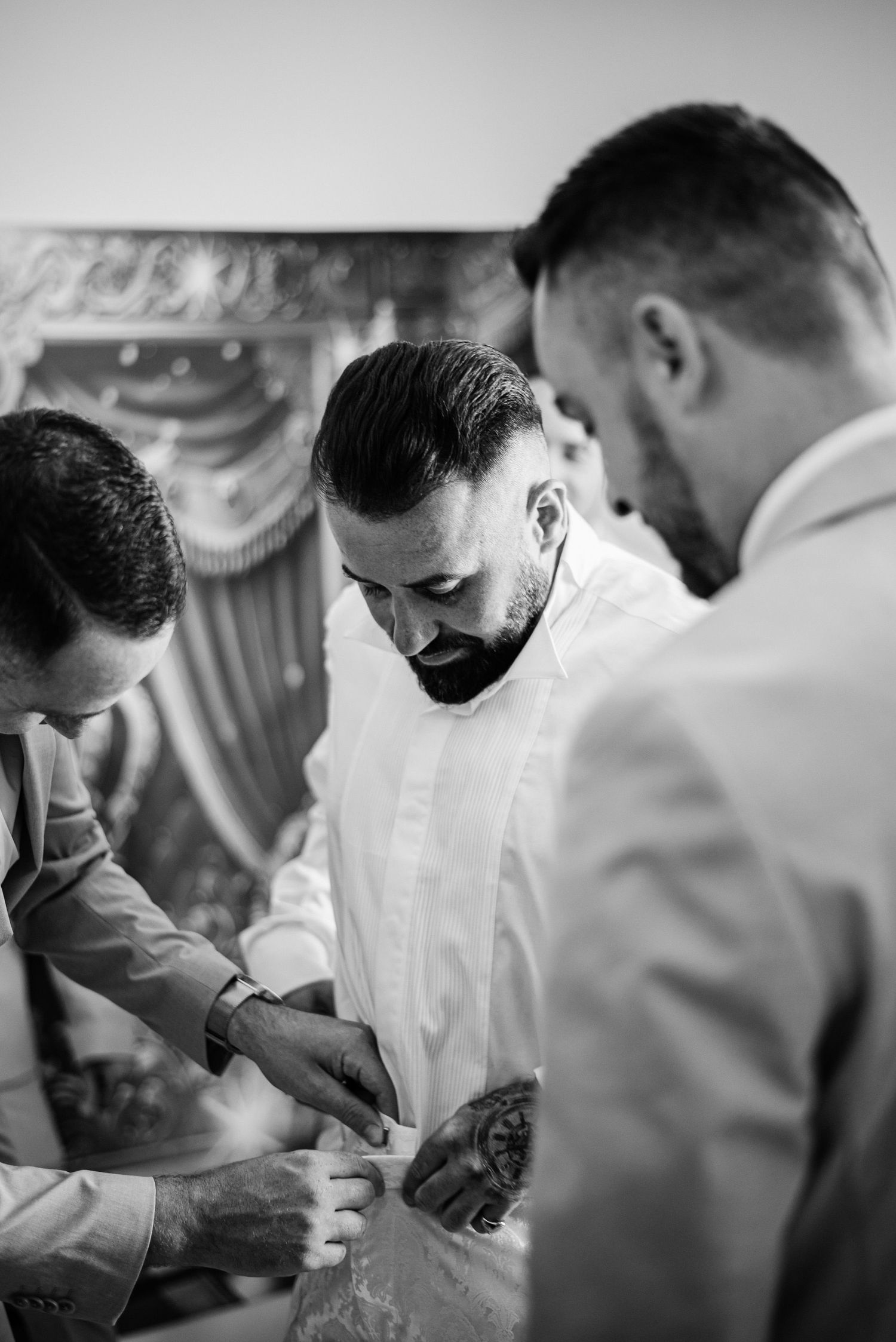 Black and white photo of groom getting cufflinks fastened by groomsmen before wedding ceremony.