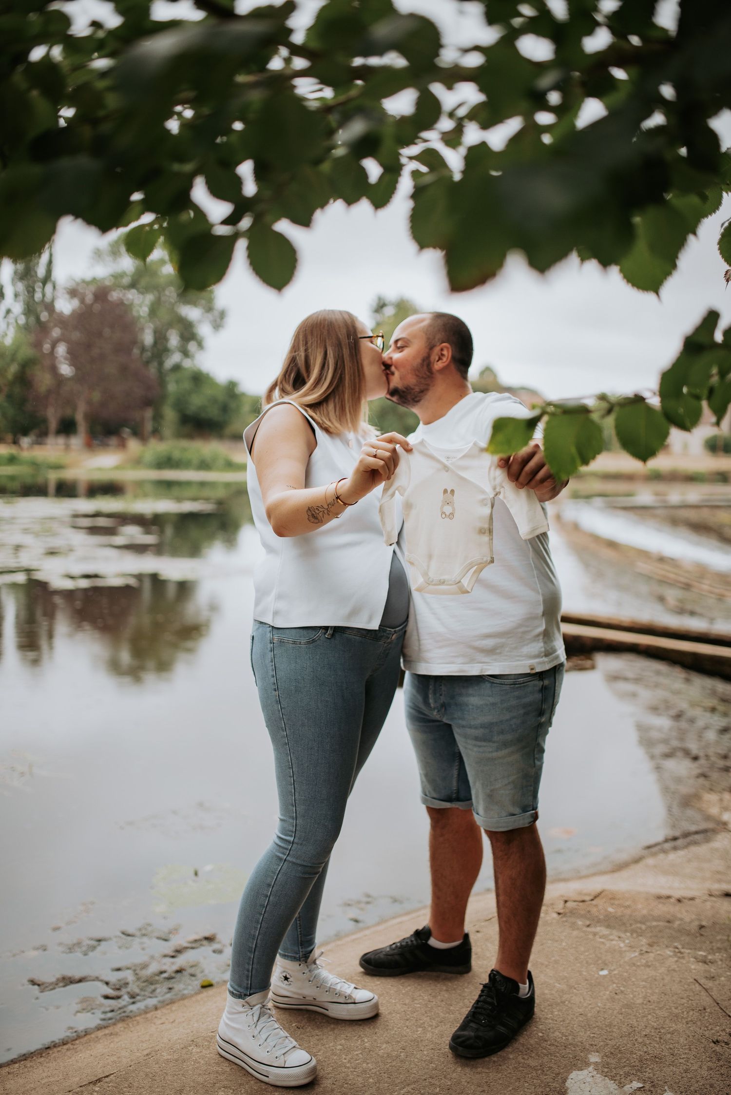 Two people in jeans share an intimate moment together by a peaceful pond in a romantic outdoor setting.