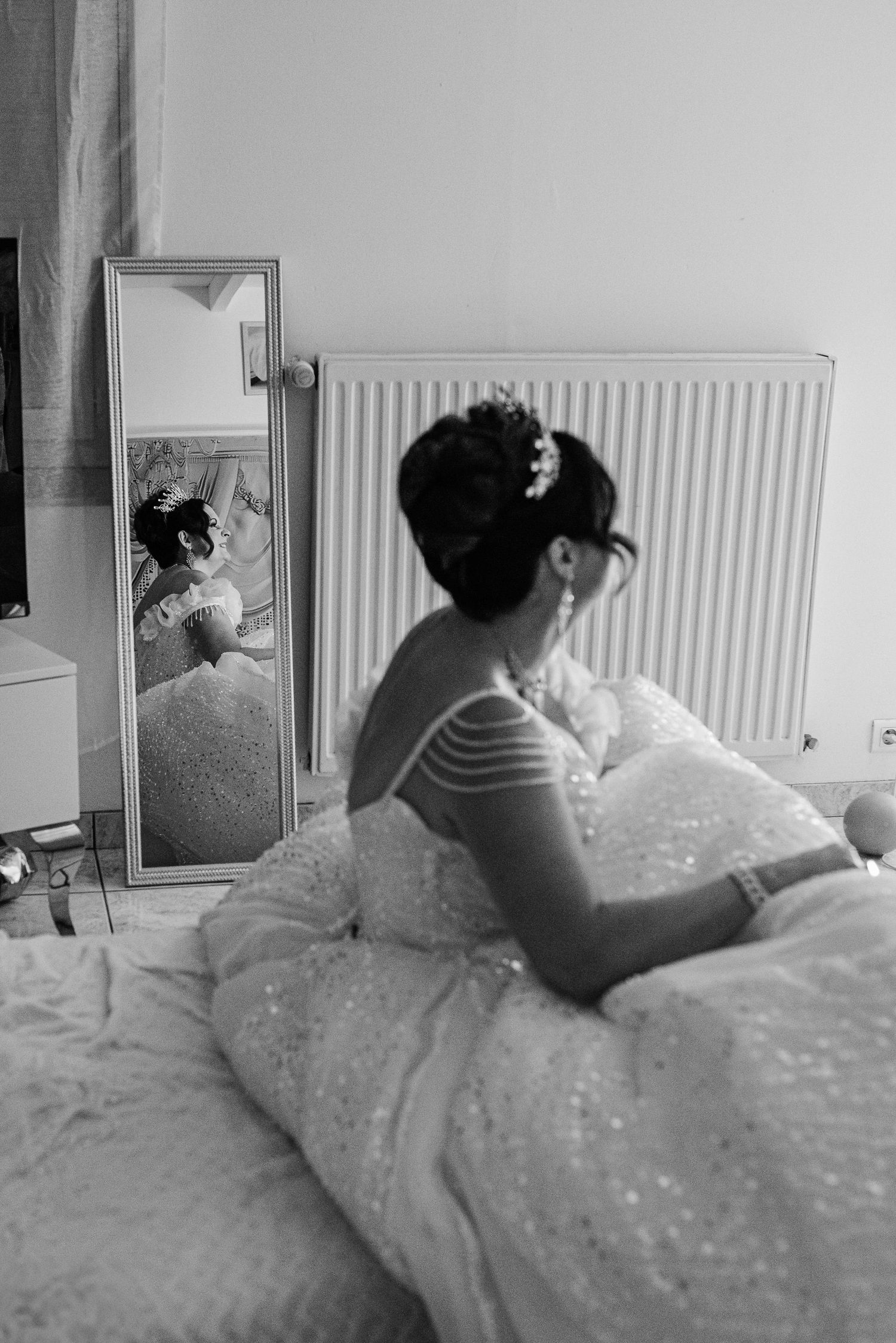 A black and white photograph shows someone in a sparkly wedding dress looking at their reflection in a mirror.