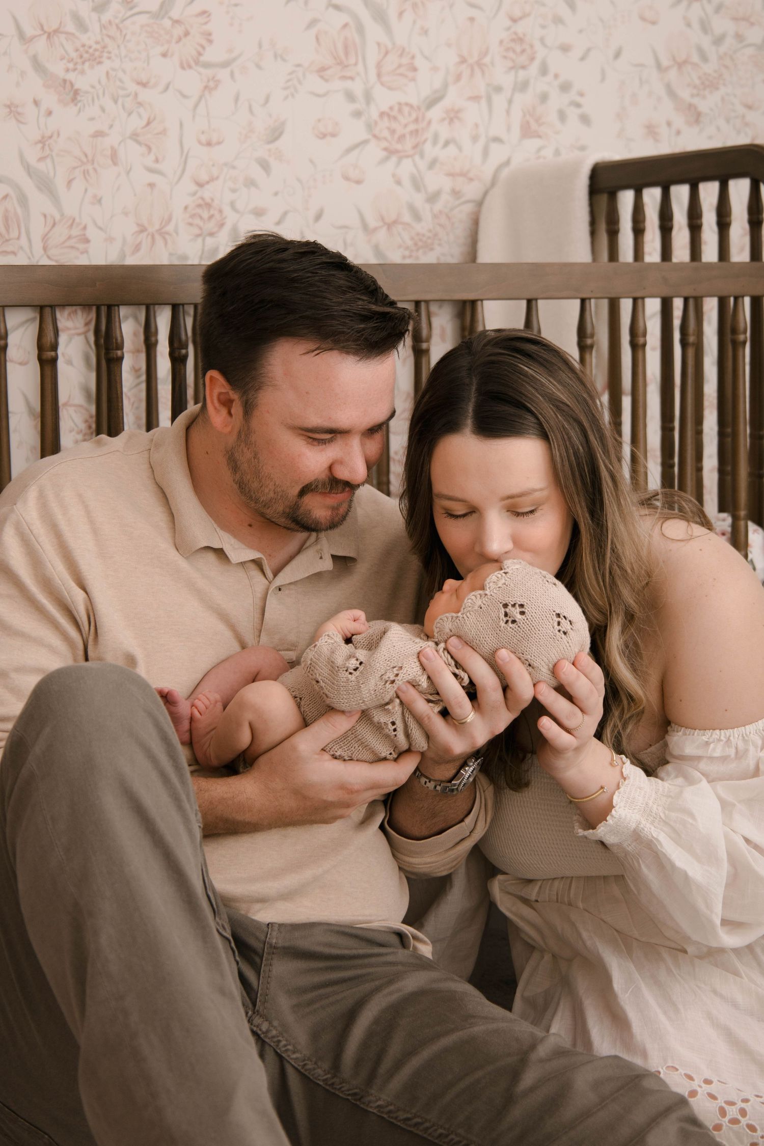 Parents share intimate moment with newborn baby while sitting by nursery crib.