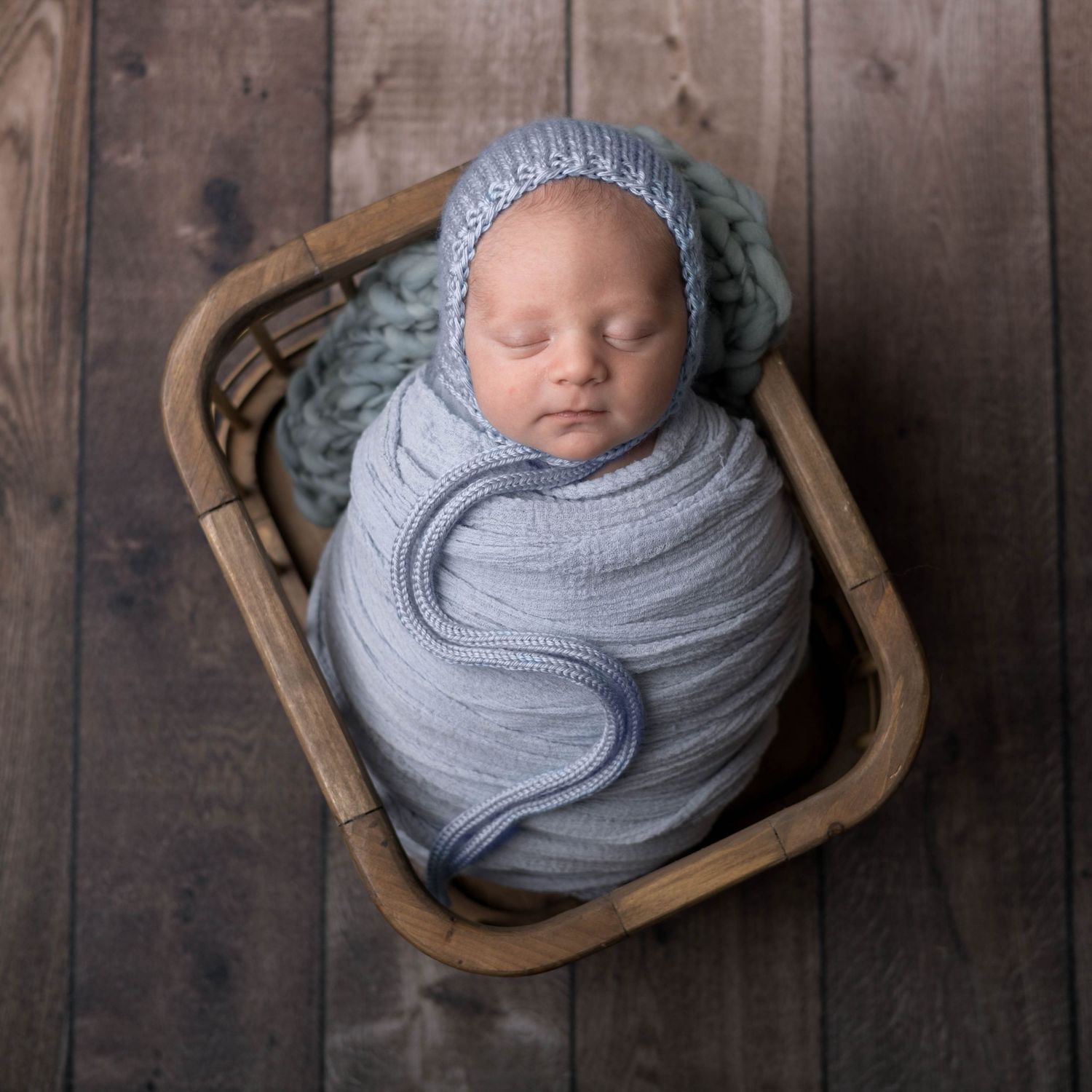 A newborn baby wrapped in soft gray swaddle cloth photographed from three different angles on a rustic wooden backdrop.