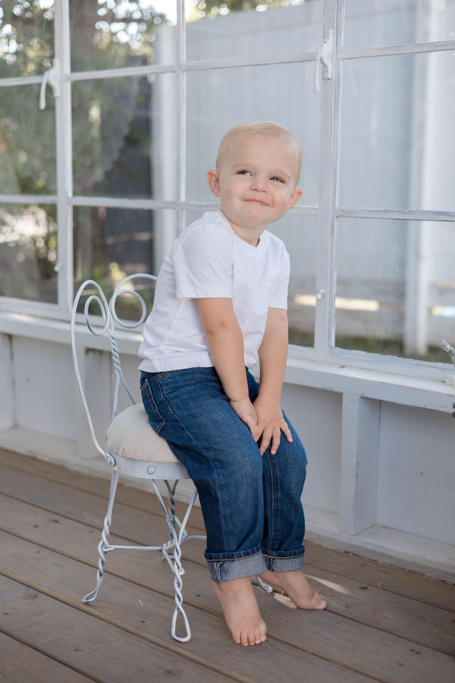 A young child in jeans and white t-shirt sits on a white porch in a series of connected photos.