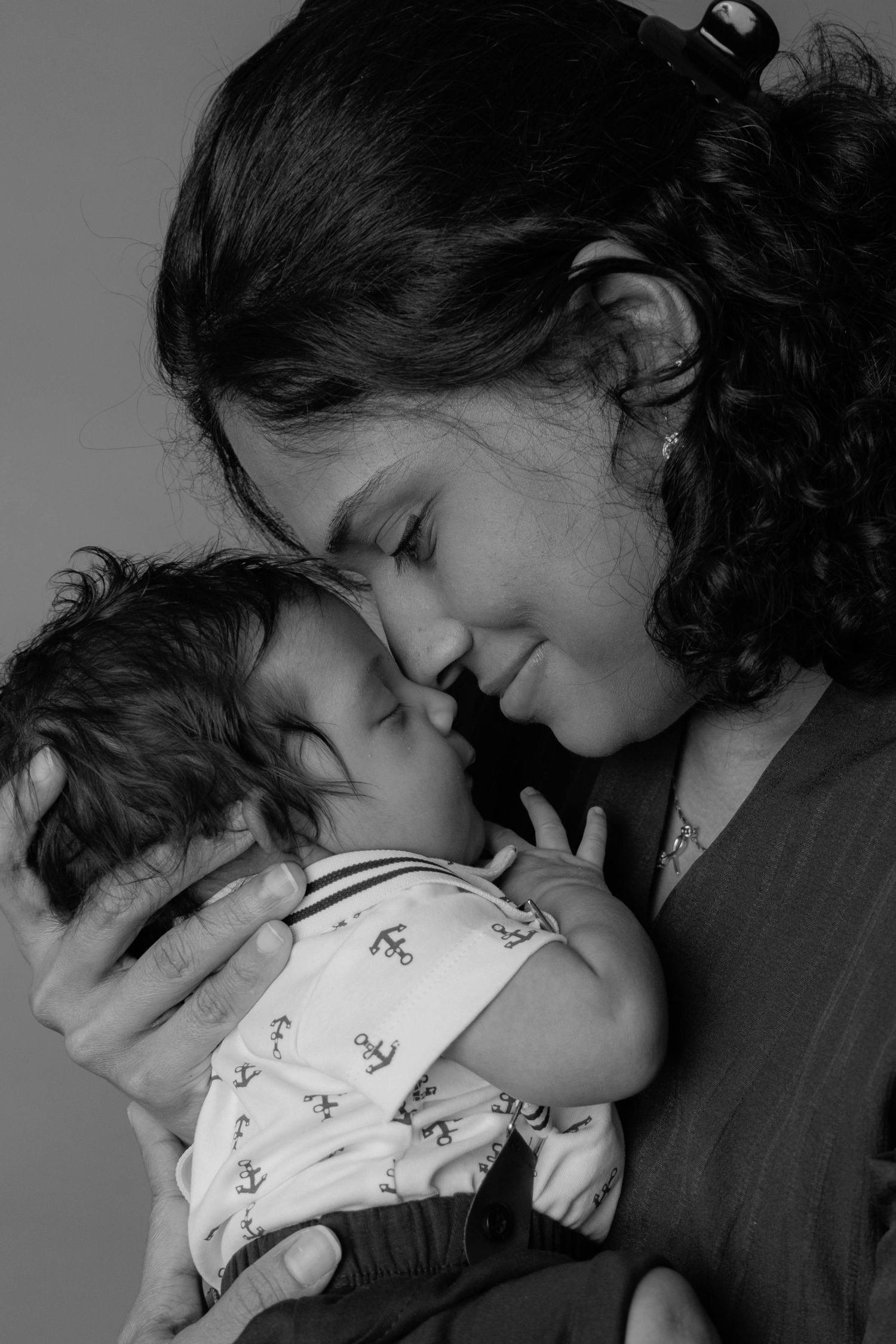 Black and white photo of a mother tenderly touching foreheads with her sleeping newborn baby.