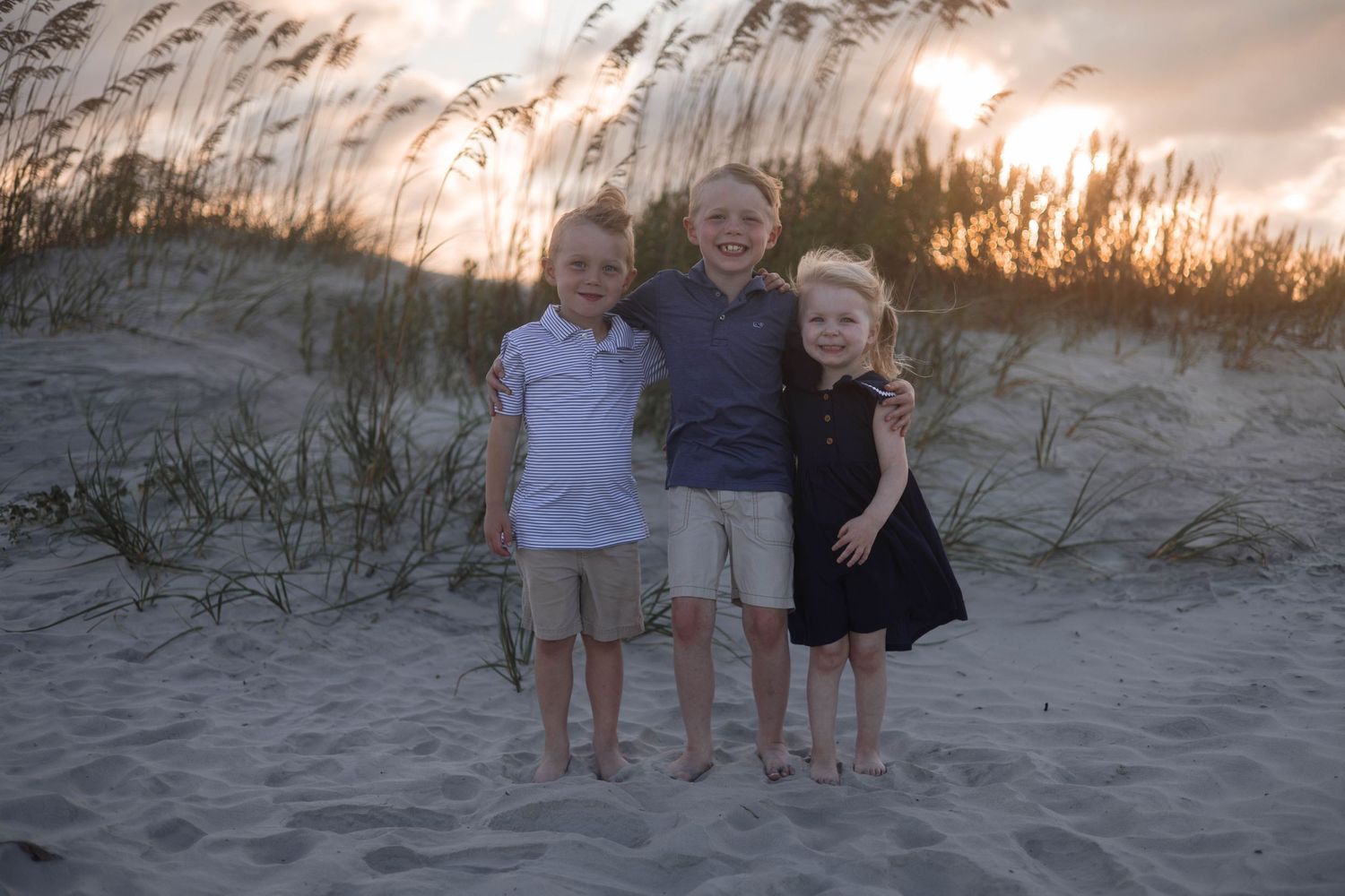 Children enjoy a playful moment on sandy beach dunes during golden hour.