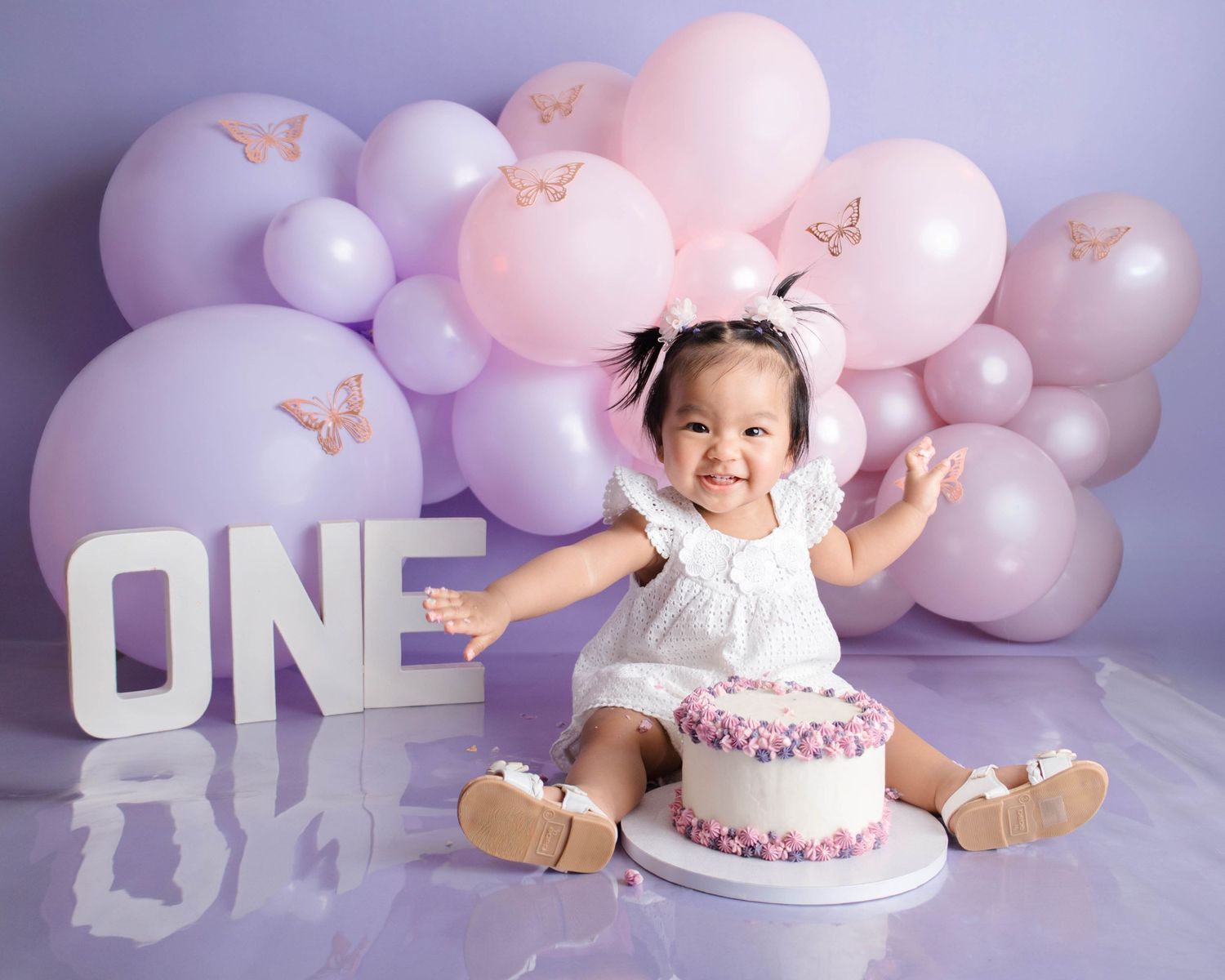 Pink and white balloon garland decorates a first birthday cake smash photo session with soft pastel colors and delicate details.