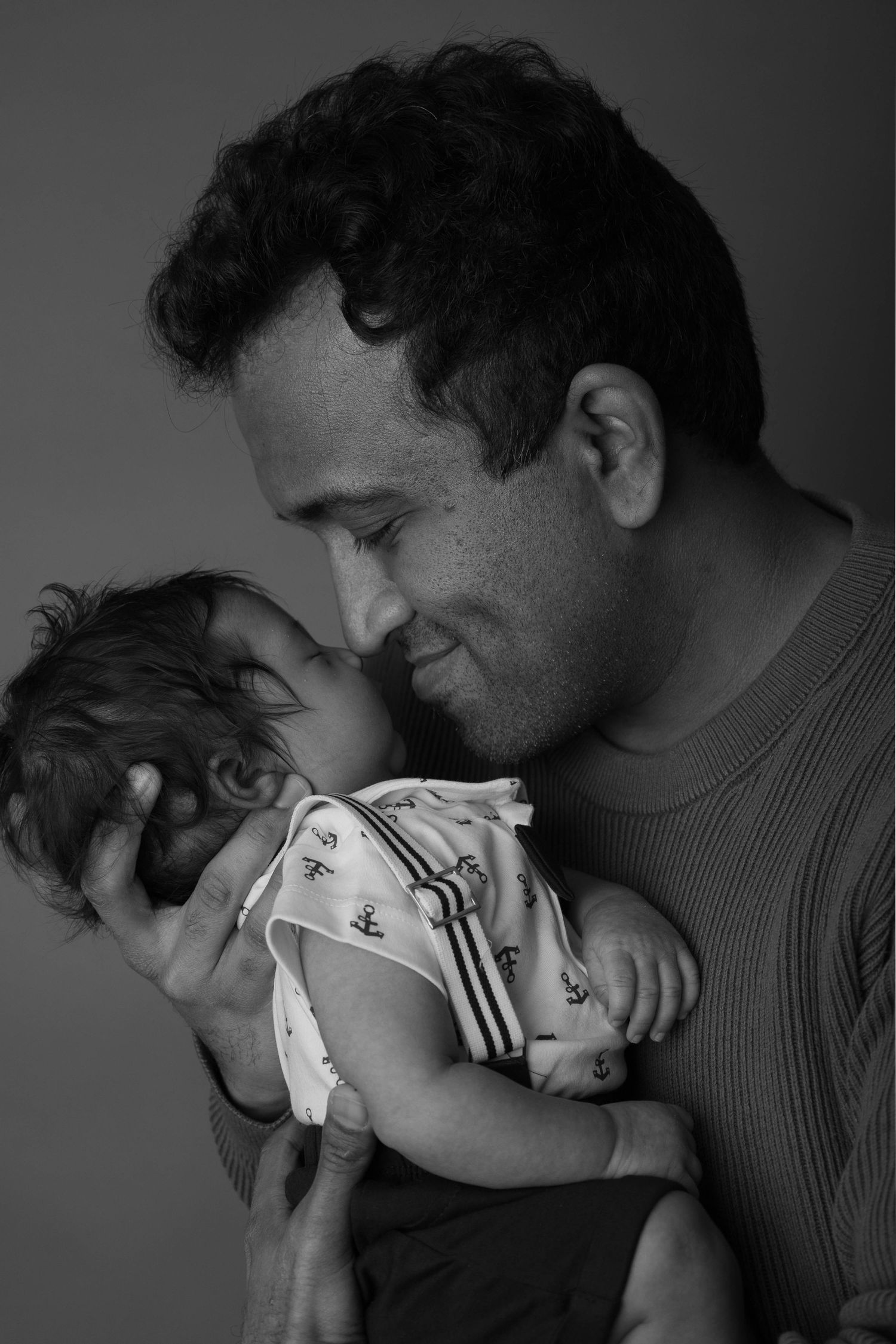Black and white portrait of a father tenderly holding his newborn baby, smiling with love and joy.