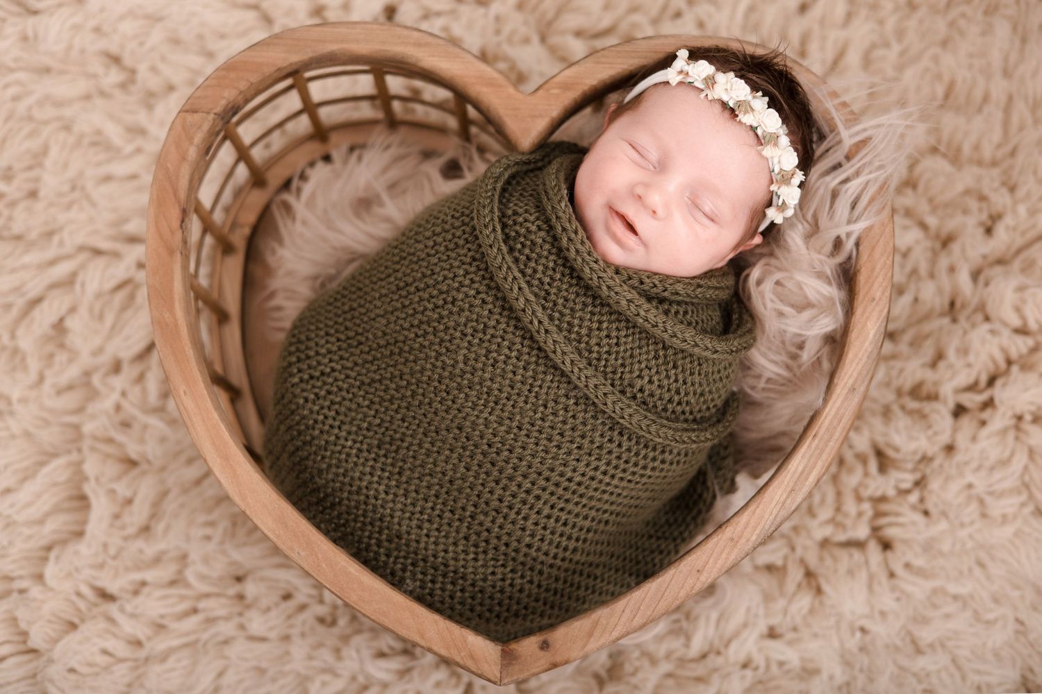 Sleeping newborn wrapped in an olive green knit blanket on textured beige background.
