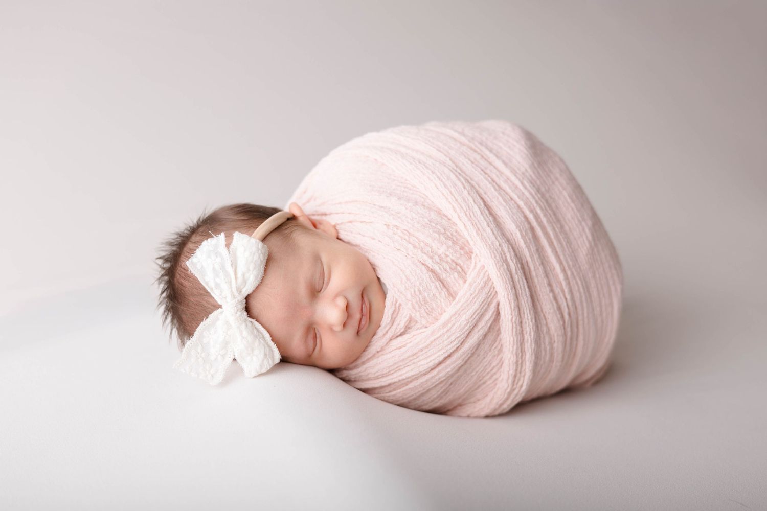 A series of soft pink newborn photography poses on a light backdrop showing wrapped baby in different angles.