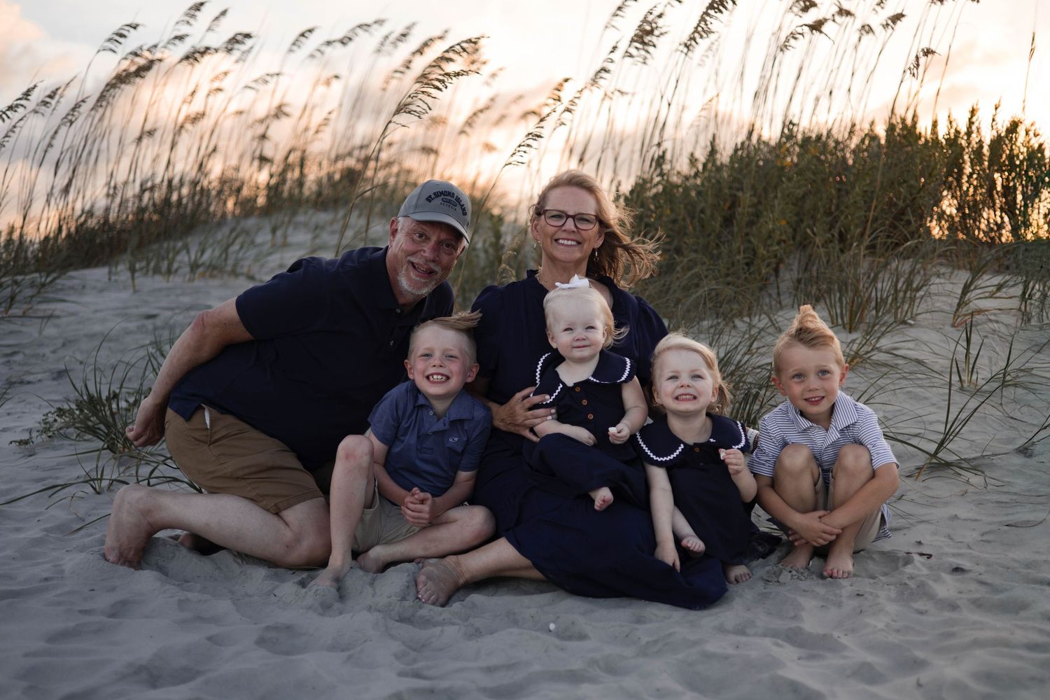 Family relaxes together on sandy beach at dusk with sea oats swaying in background.