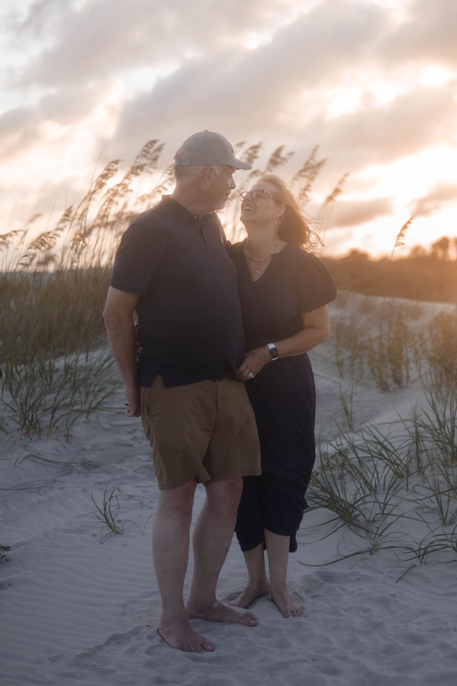 A romantic sunset portrait on sandy dunes with sea oats swaying in the background.