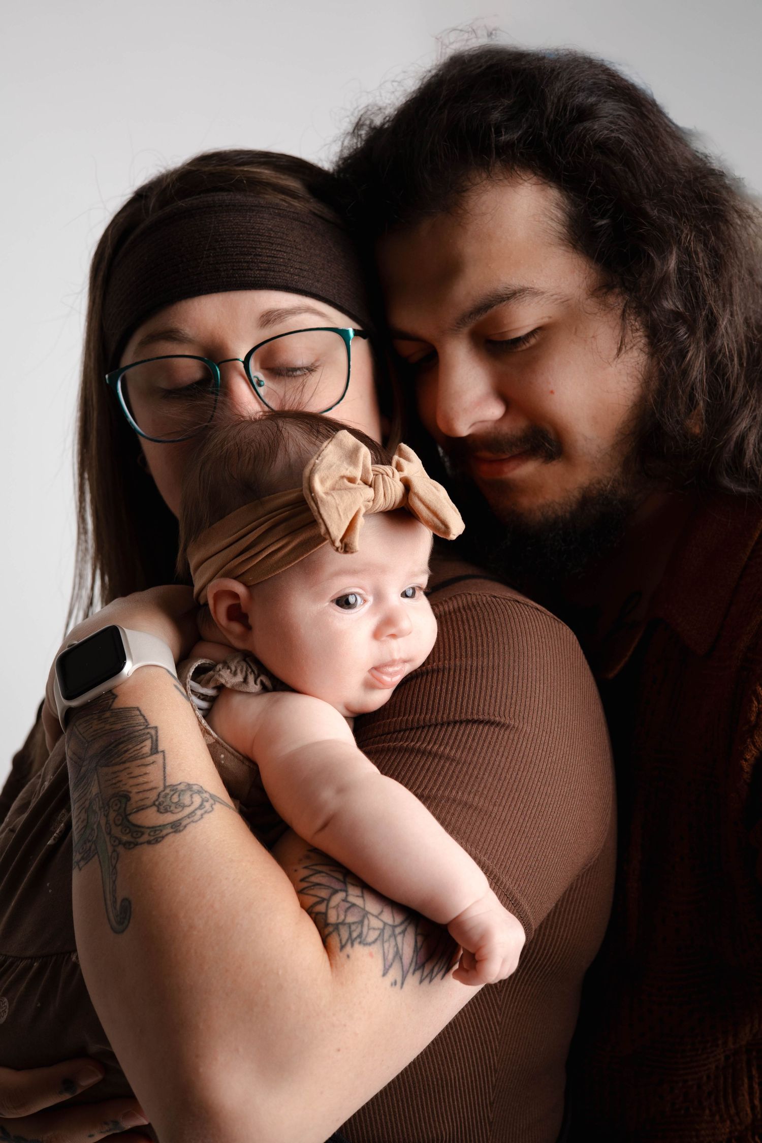 Parents sharing gentle moments with their baby in studio portraits against grey backdrop.