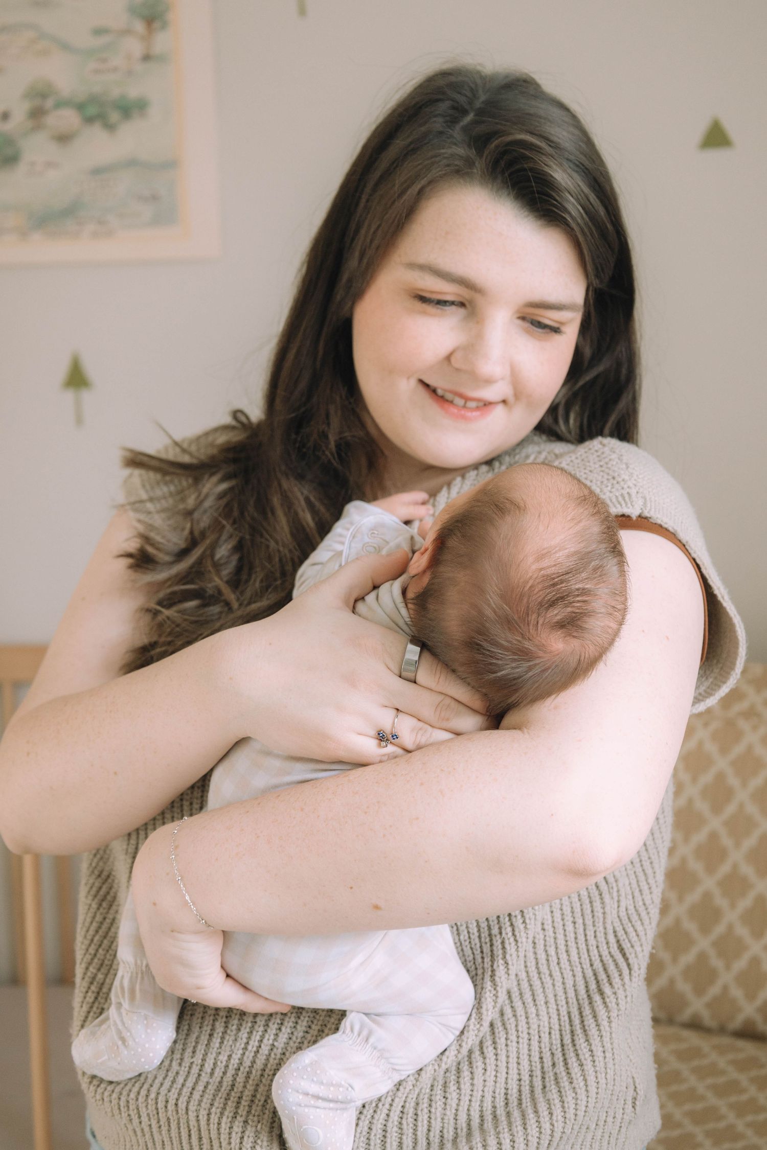 Smiling young mother with dark hair gently cradling her newborn baby in a softly lit nursery room.