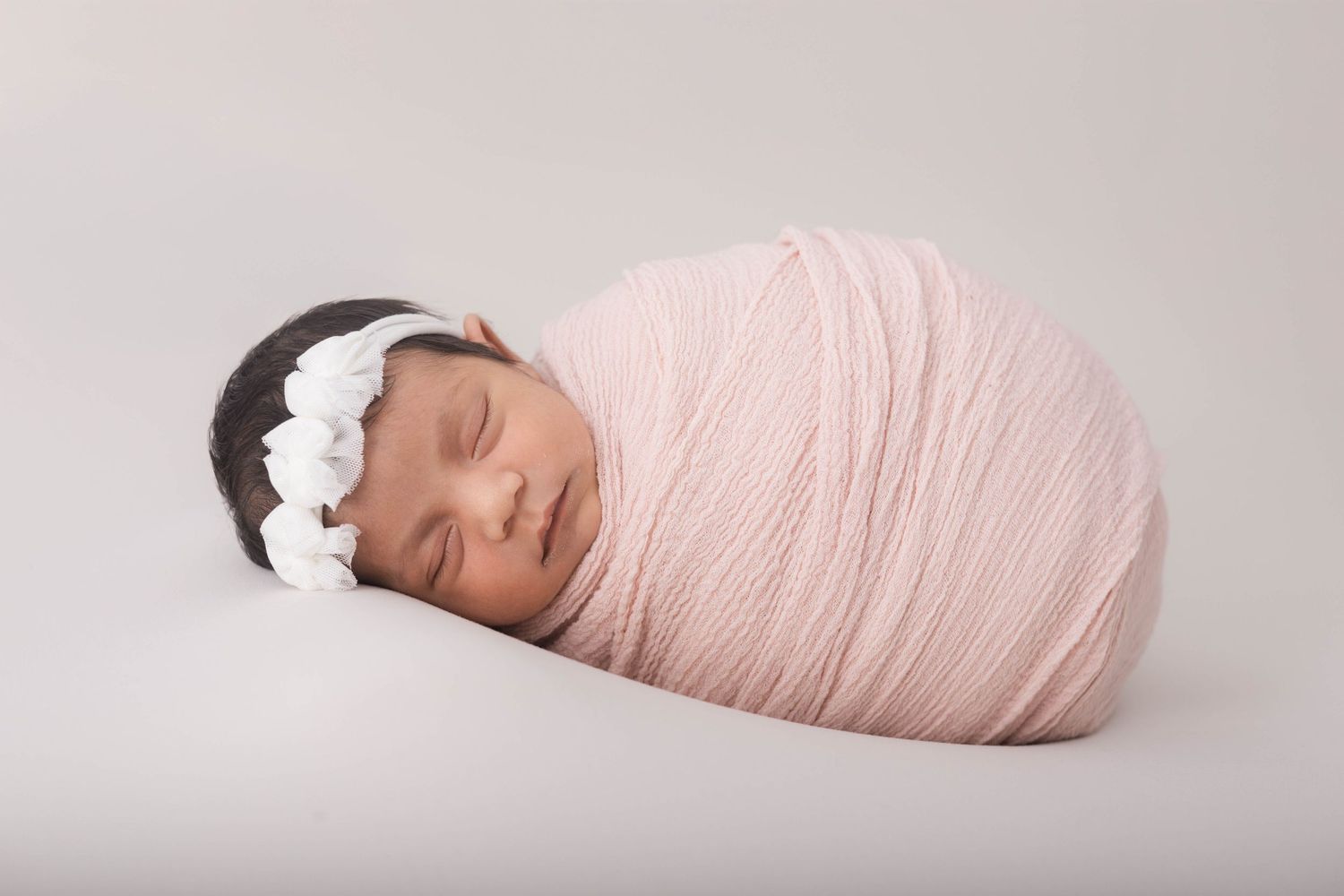 A series of newborn photography poses showing a baby wrapped in soft pink fabric against a light gray background.
