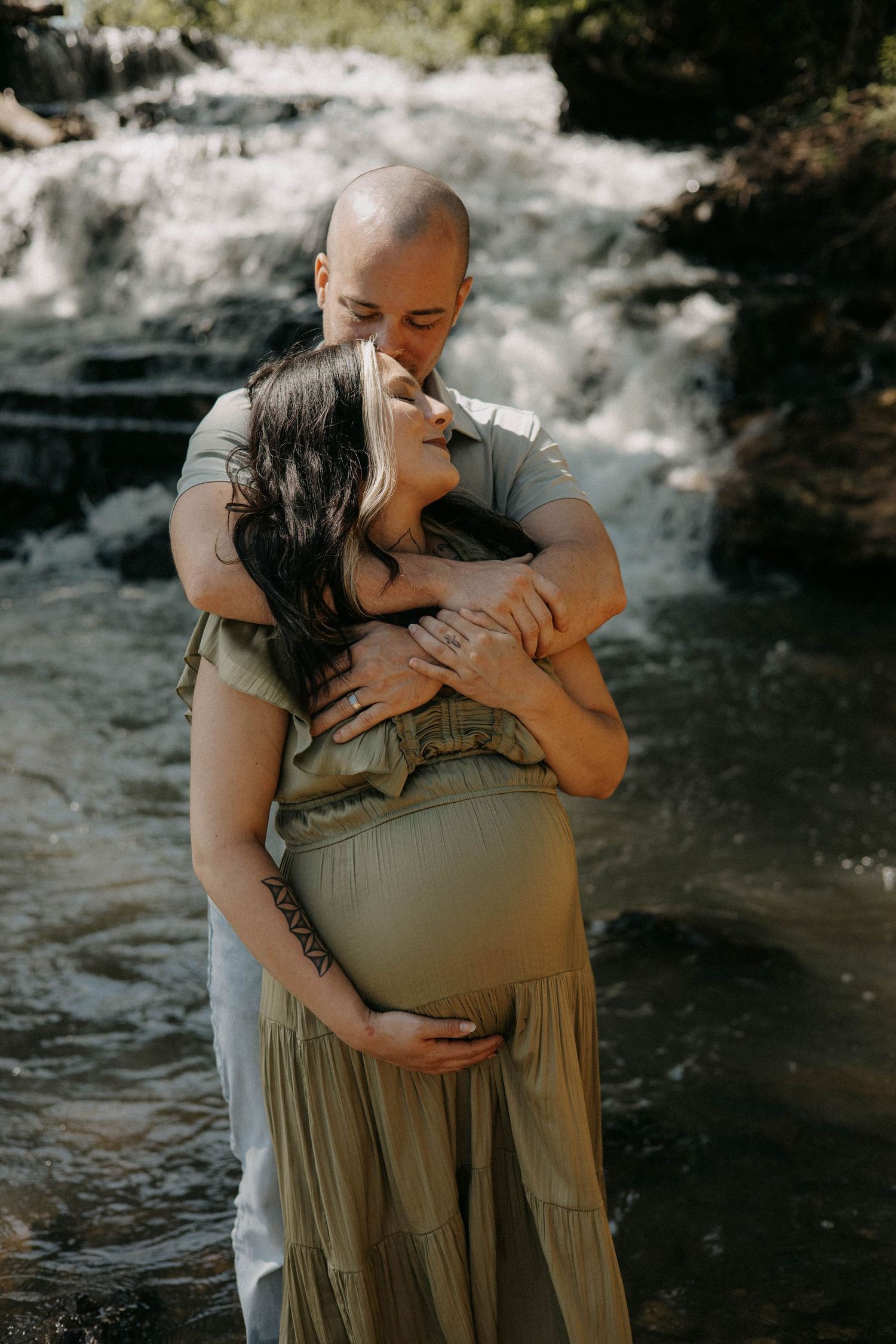 A tender embrace captured in front of a waterfall during a maternity photo session.