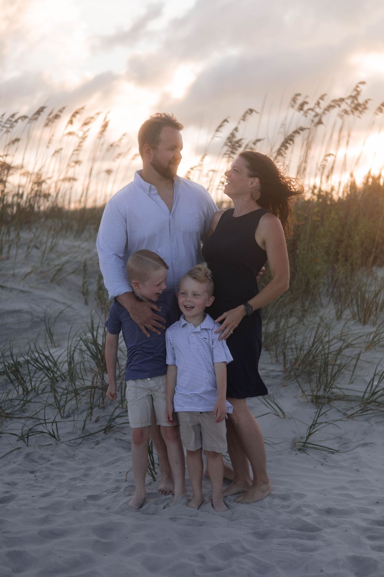 A family portrait at sunset on beach dunes with sea oats silhouetted against the sky.