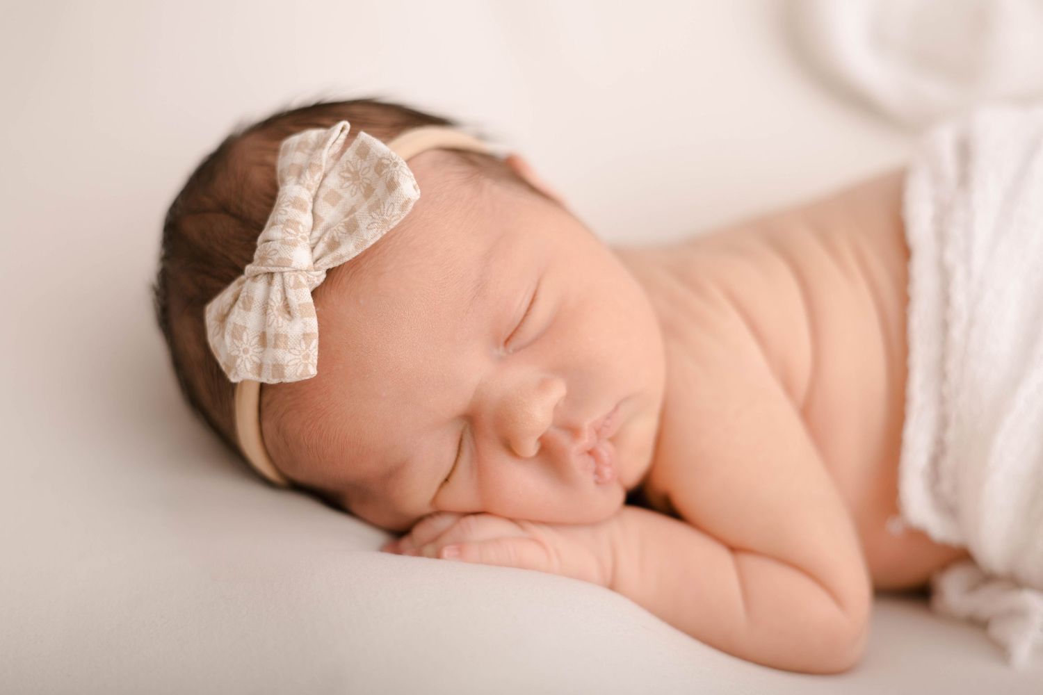 Peaceful sleeping newborn with lace bow headband on light background.