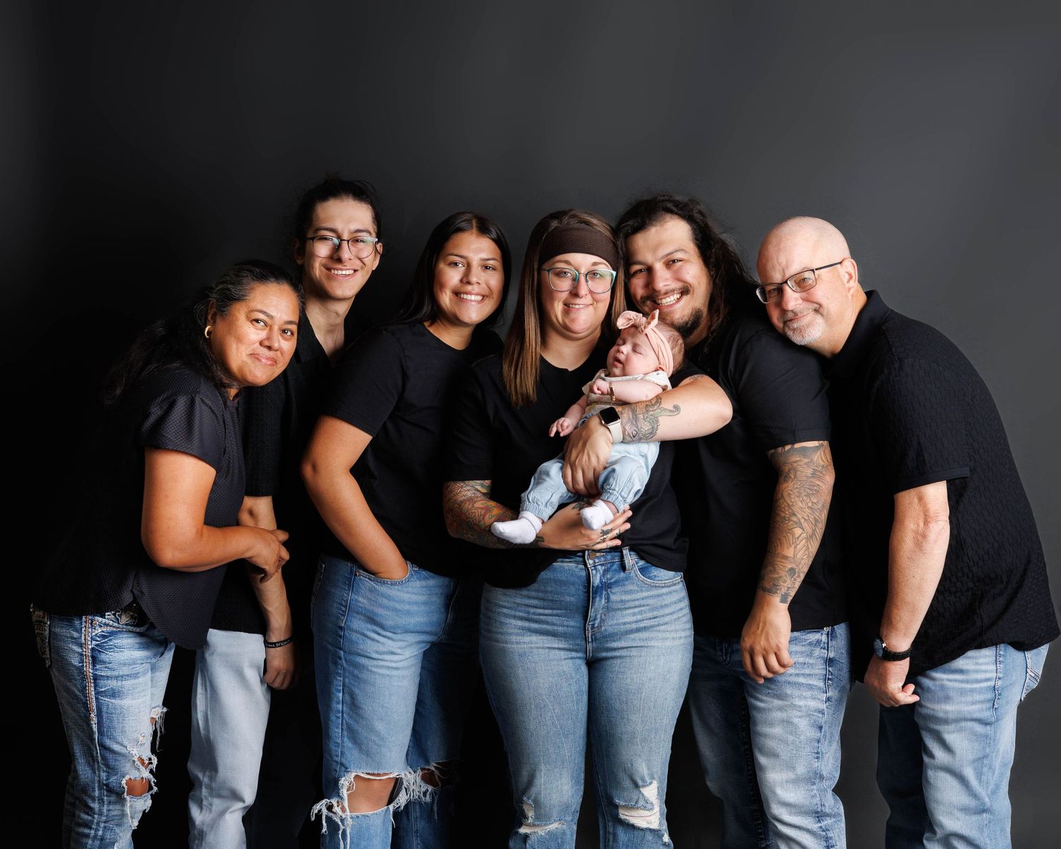 Casual family group photo session with members in jeans and black shirts against dark background.