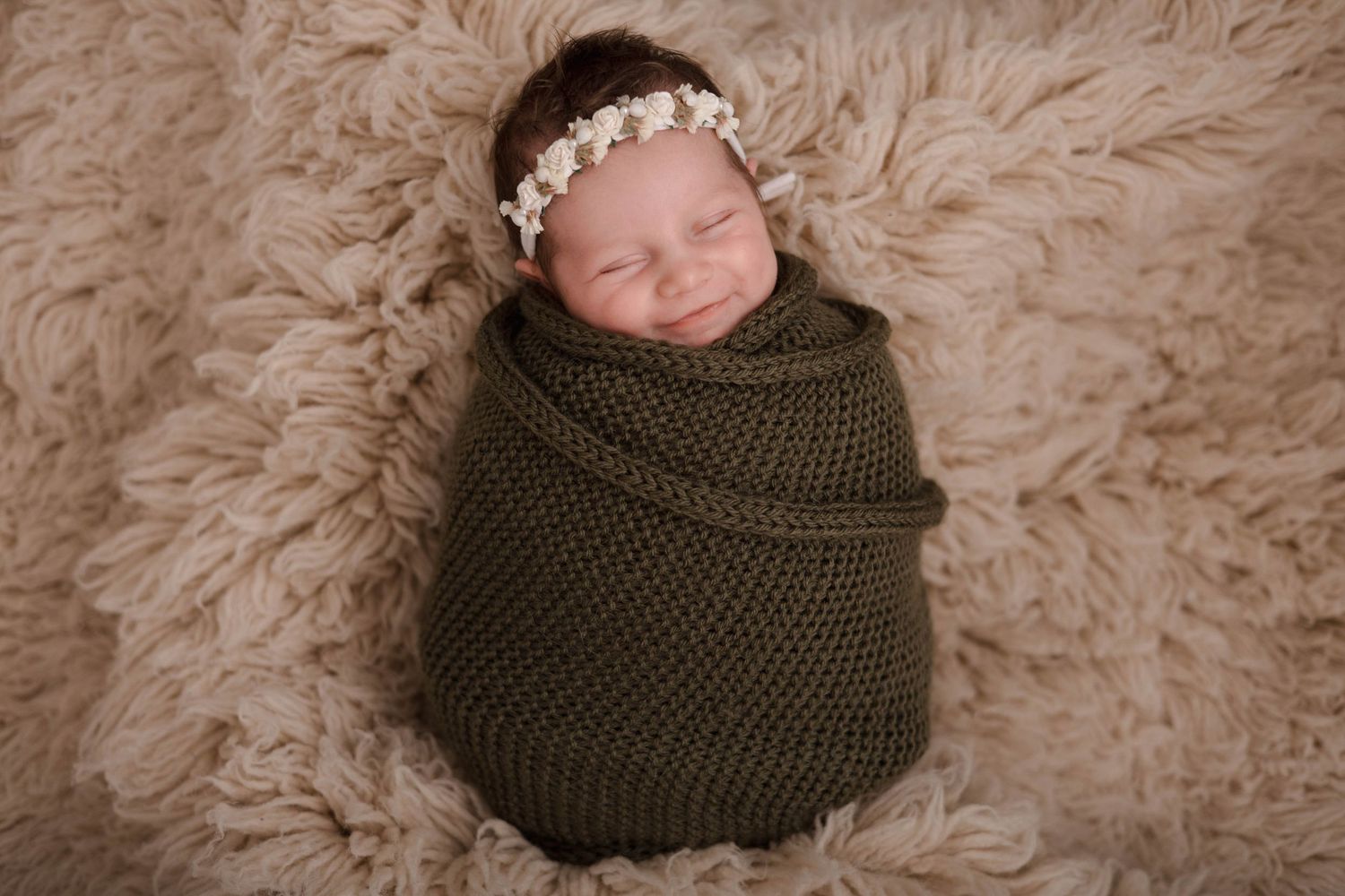Professional newborn photography with baby in wooden bowl and green knit wrap.
