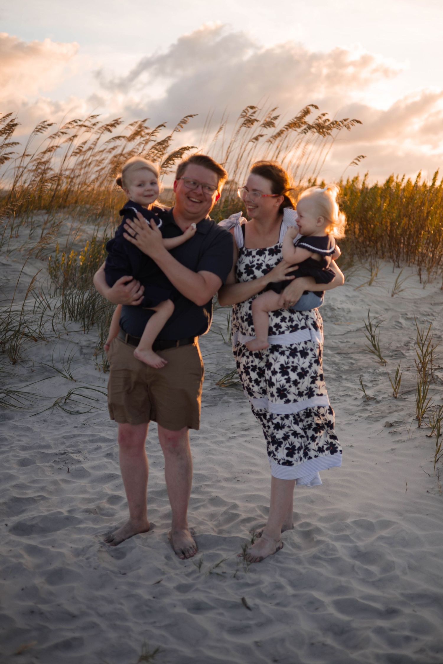 Family members share joyful moments together on coastal sand dunes during sunset.