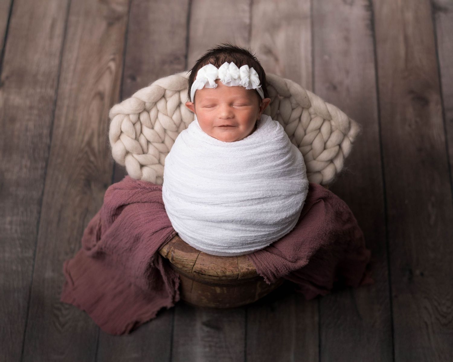 A series of four artistic newborn photography portraits with white wraps against a dark wood background.