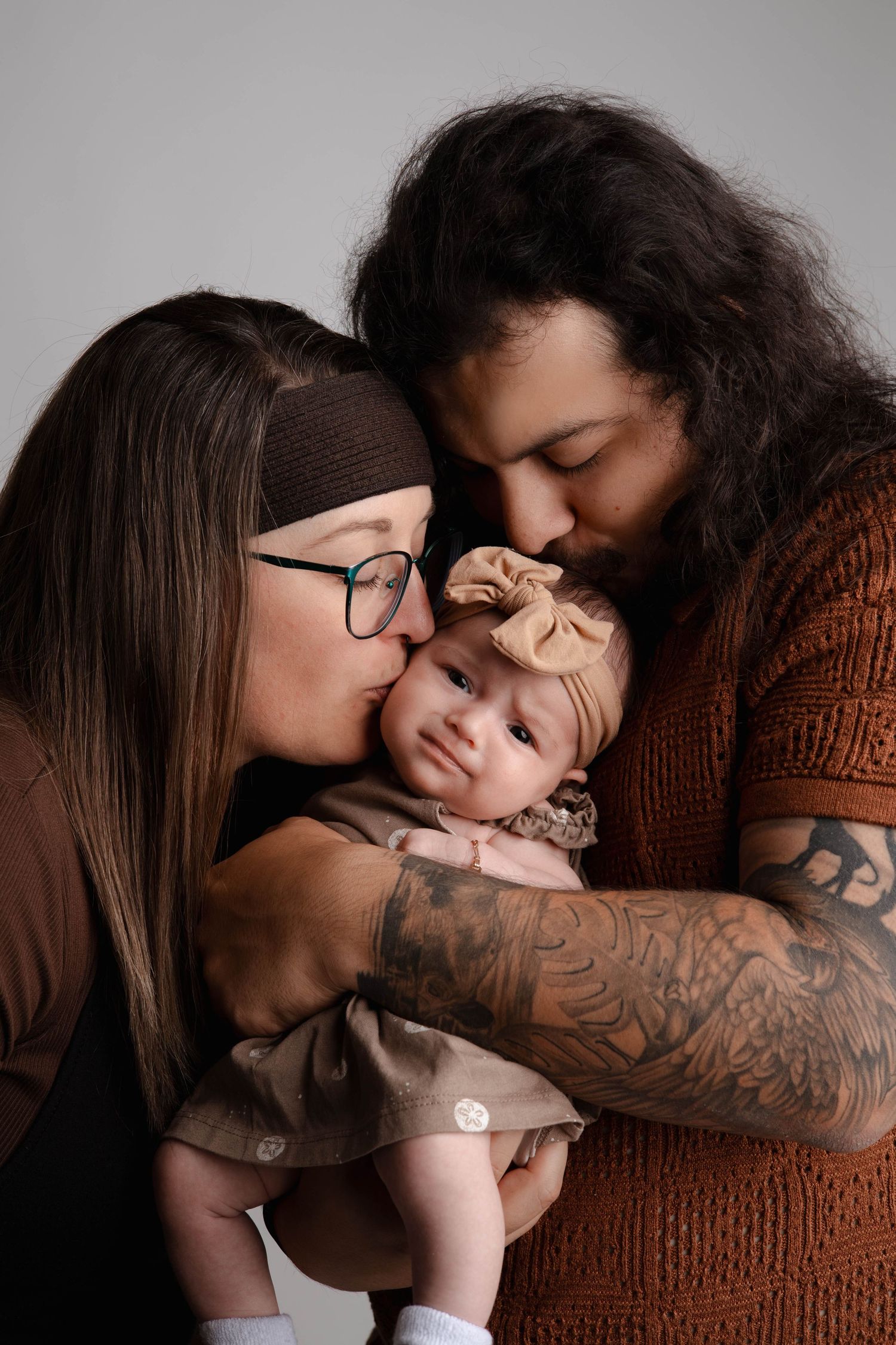 Intimate family portrait series showing tender moments between parents and baby on grey background.