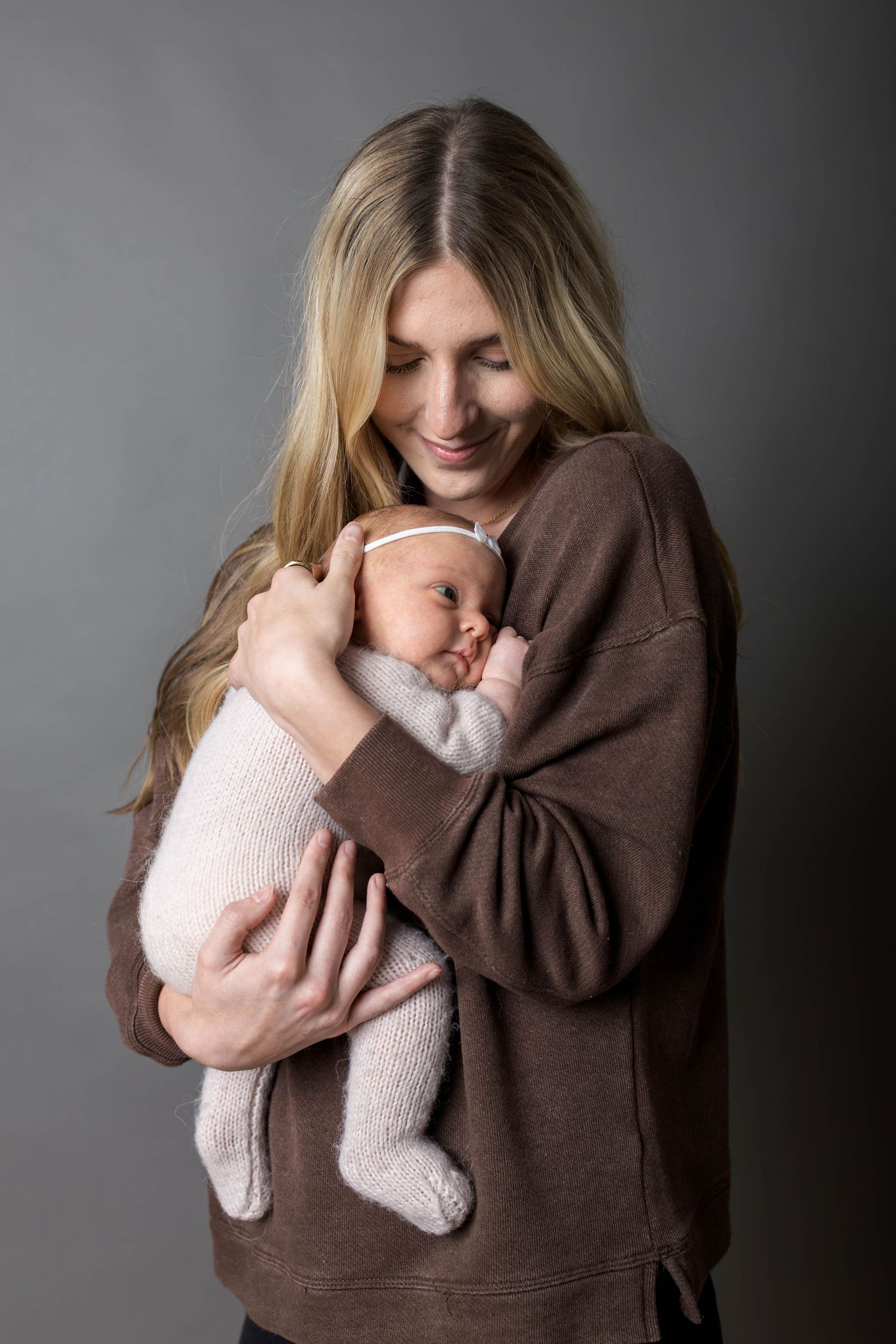 Happy mother tenderly holding her swaddled newborn baby close to her chest in a professional studio portrait.